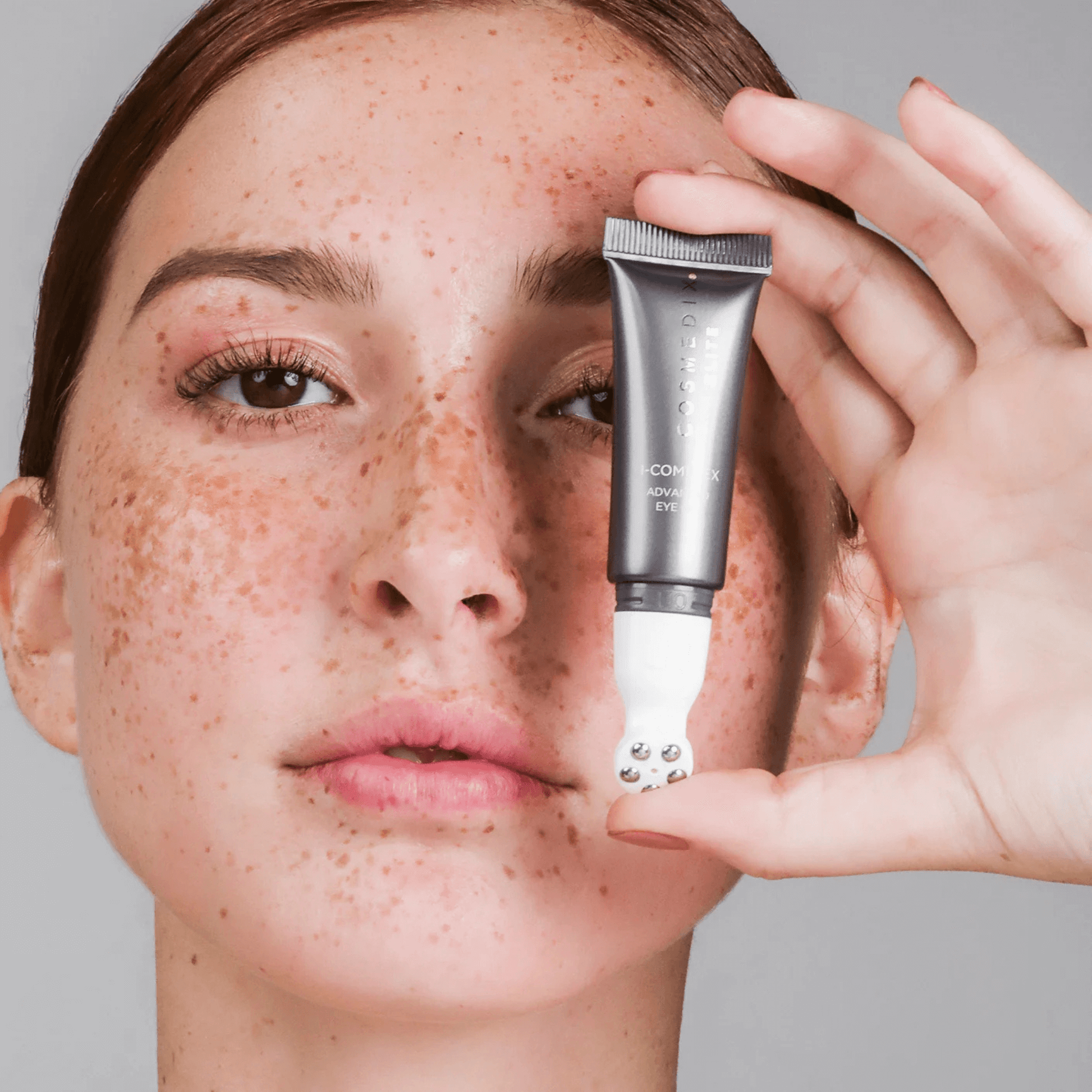 Model holding Cosmedix Elite I-complex in front of face on light grey background