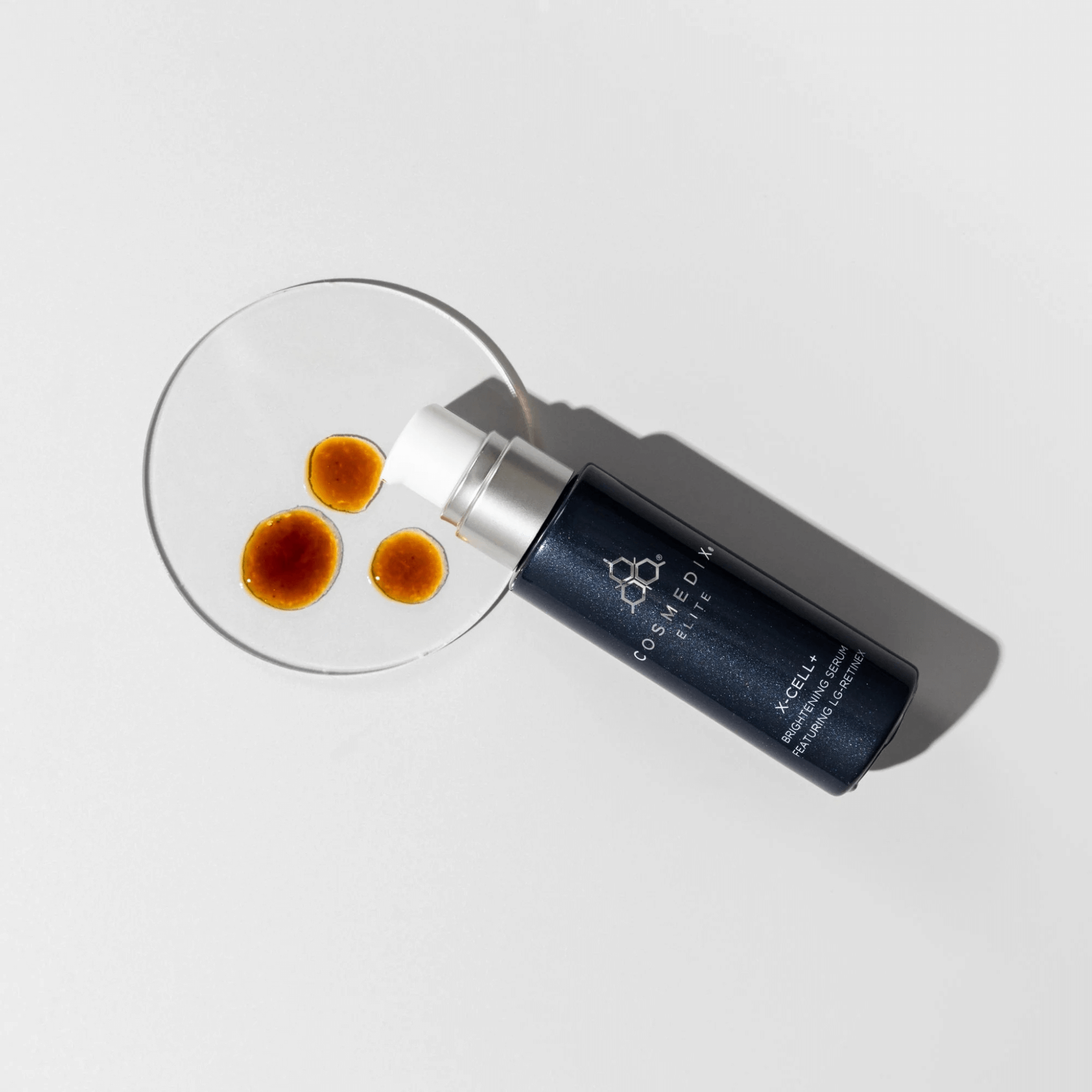 Cosmetic bottle with over a petri dish with drops of X-cell+on a light grey background