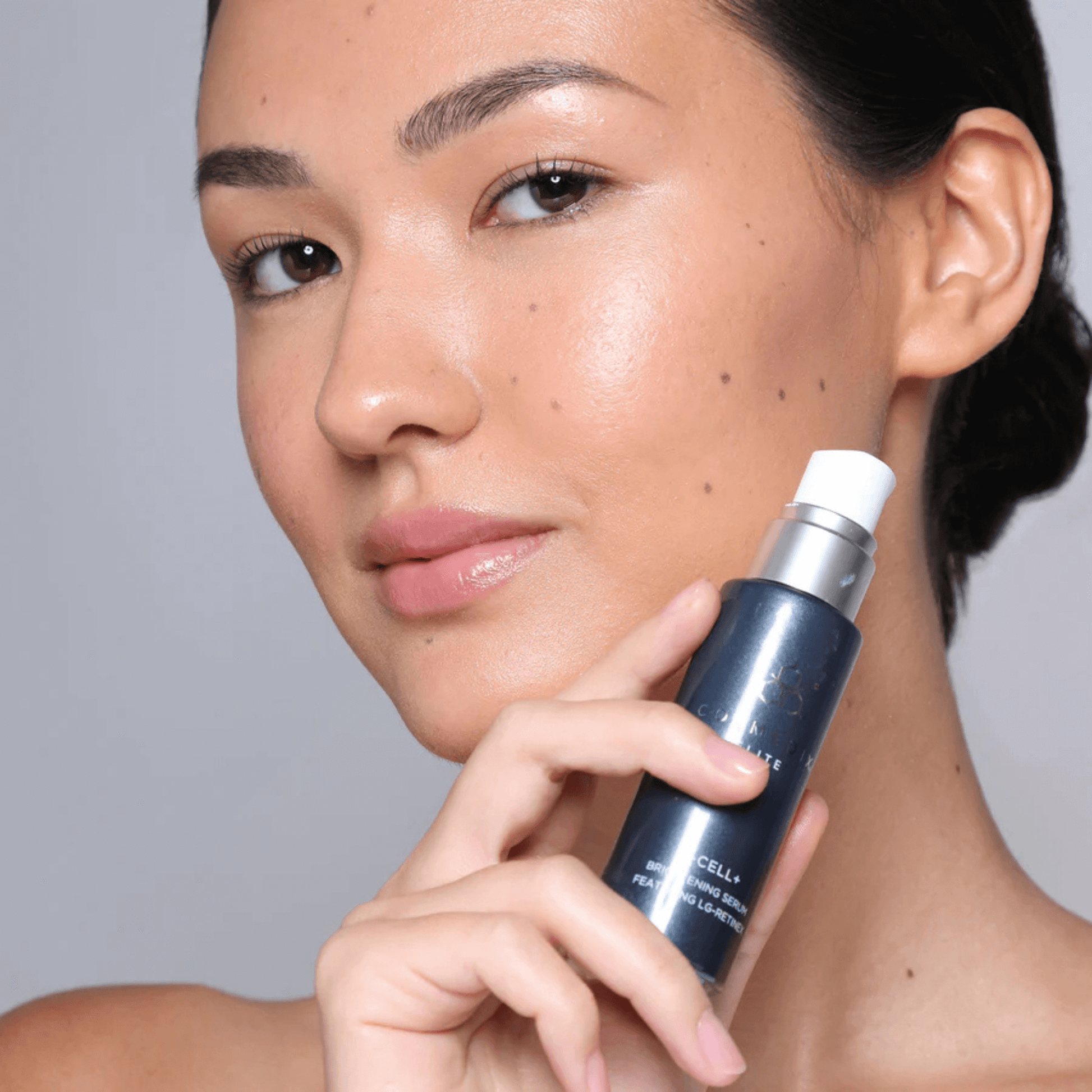 Woman holding a bottle of X-cell+ skincare against her face with a grey background