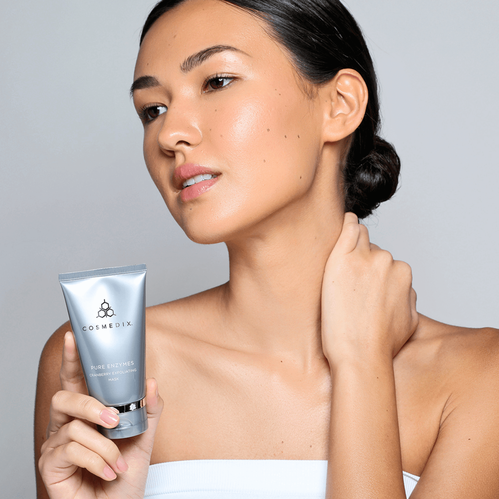 Woman holding a Cosmedix Fruit enzyme mask product against a neutral background