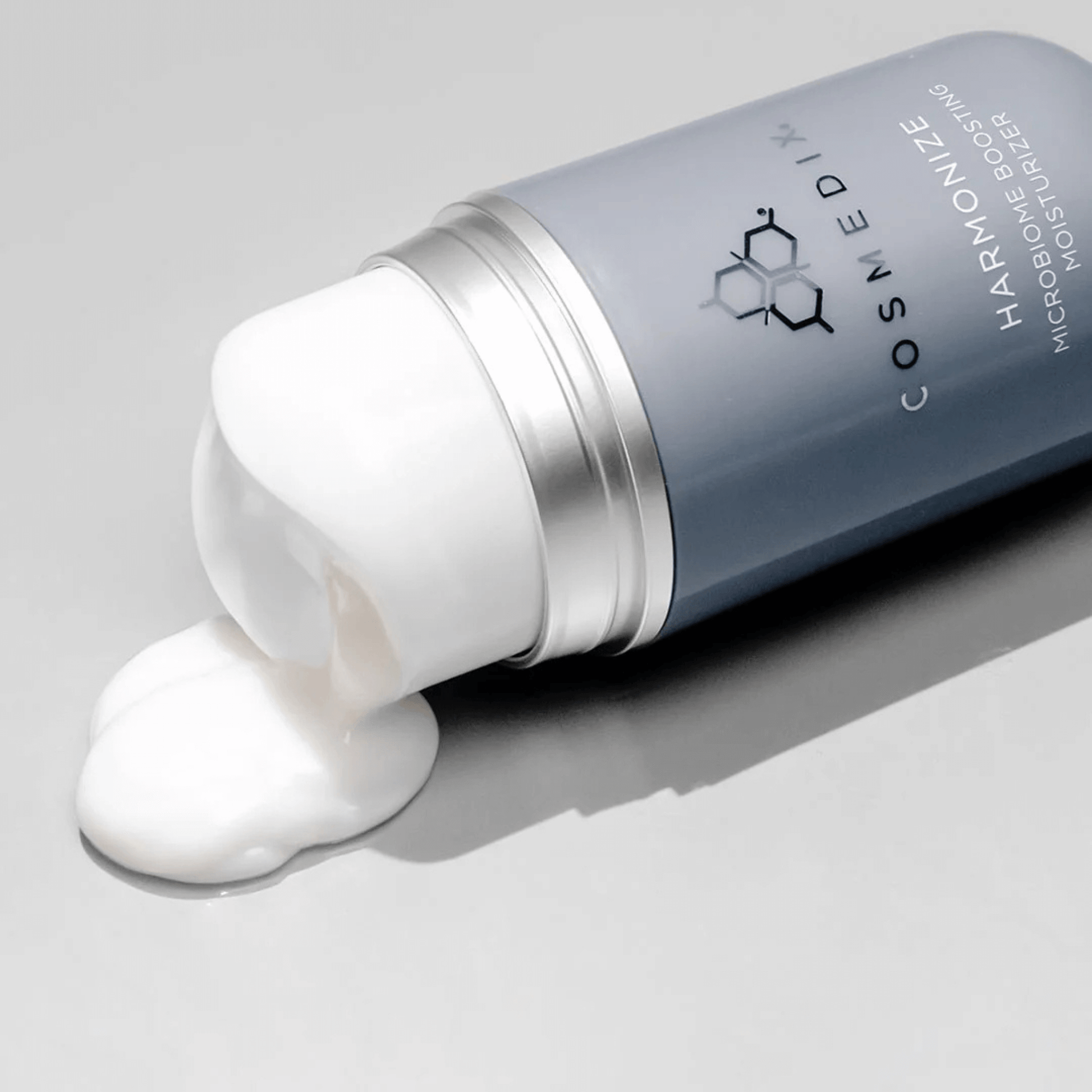 Cosmedix harmonise moisturiser tipped over with white cream on a grey background