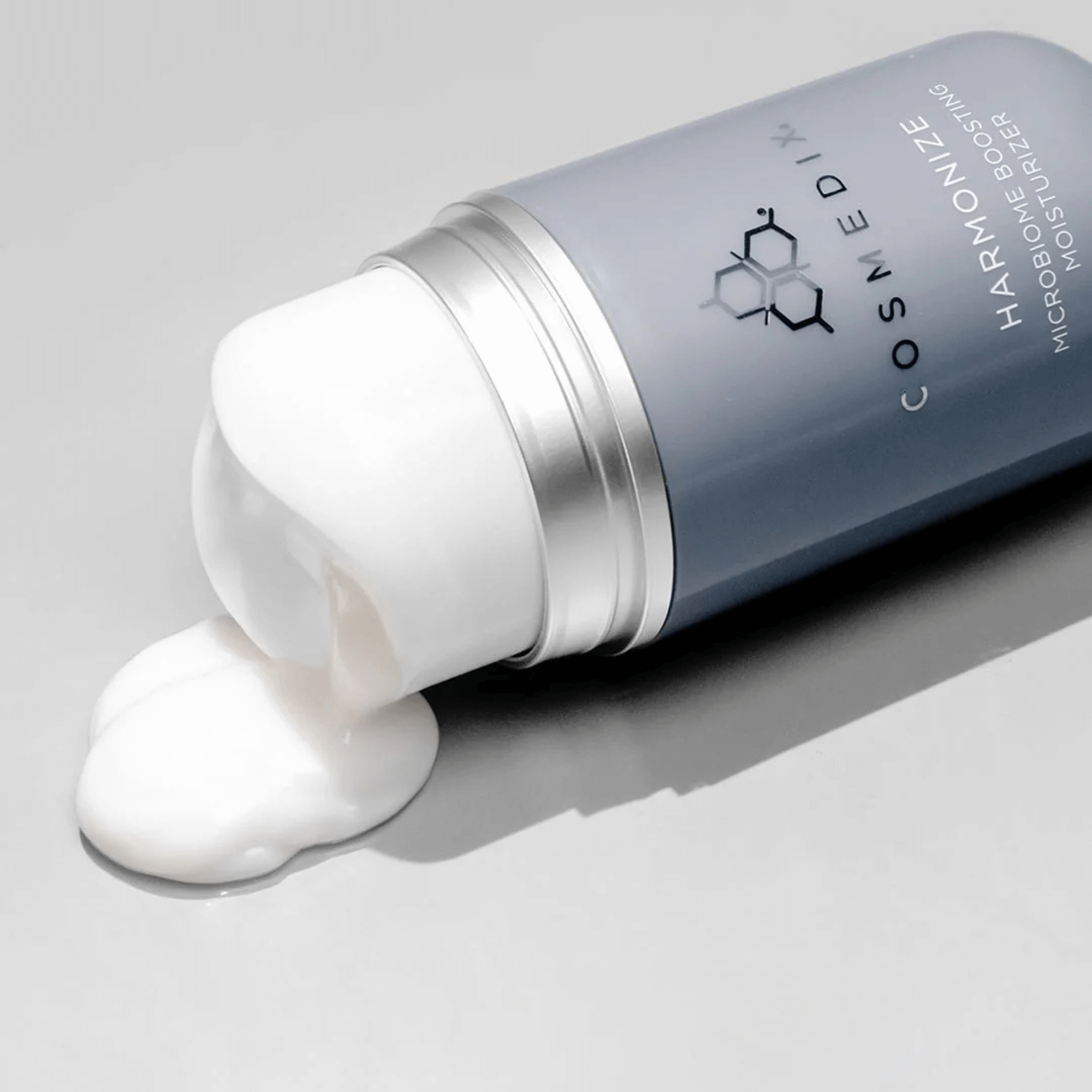 Cosmedix harmonise moisturiser tipped over with white cream on a grey background