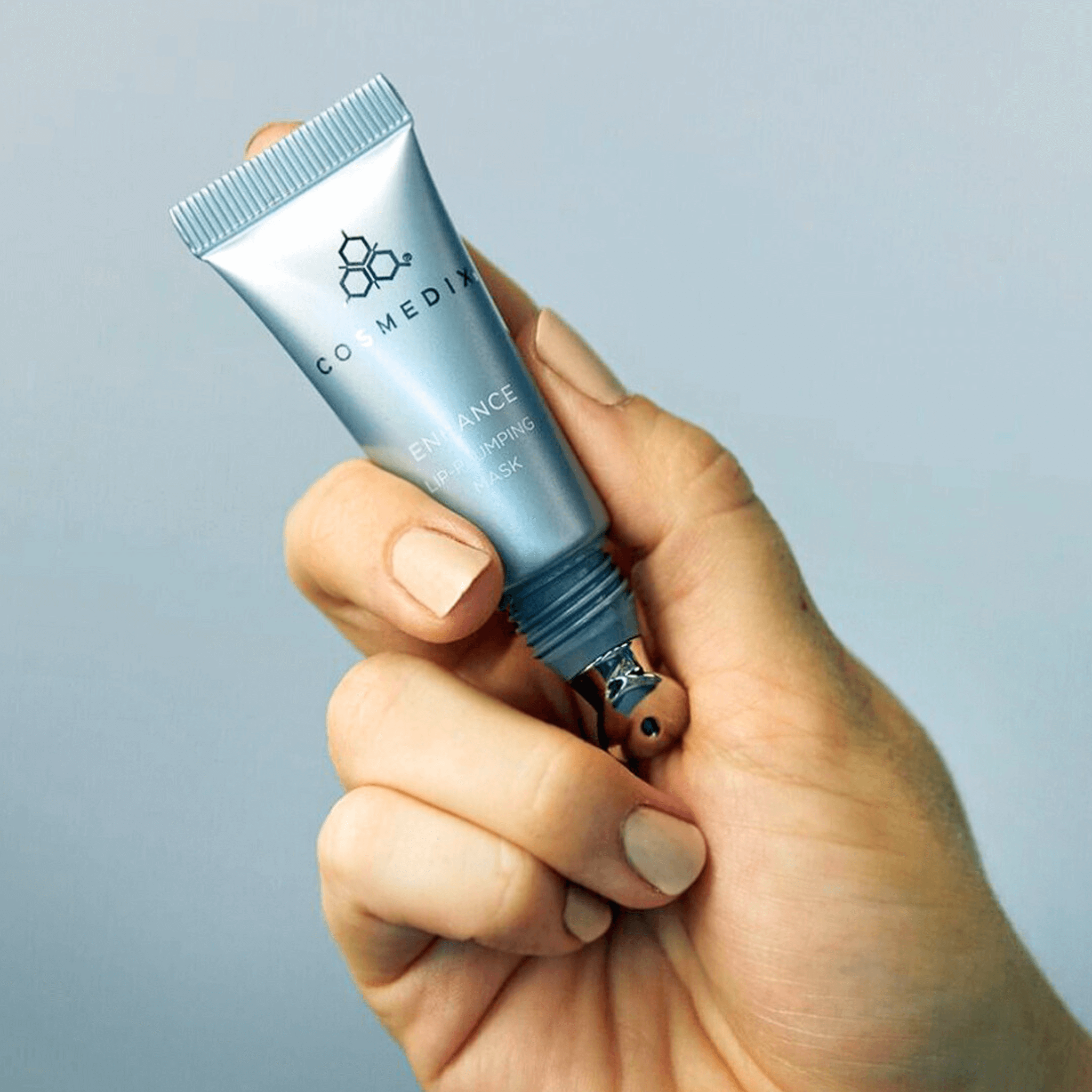 Hand holding a Cosmedix enhance tube against a light grey background
