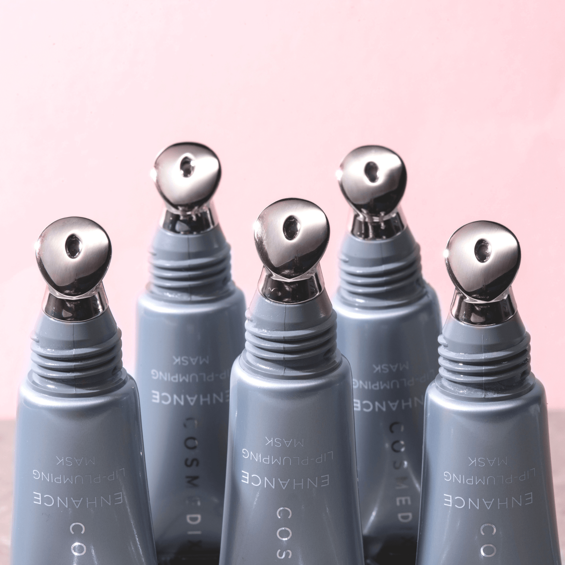 Set of five cosmedix enhance lip balm applicators with silver tips on a pink background