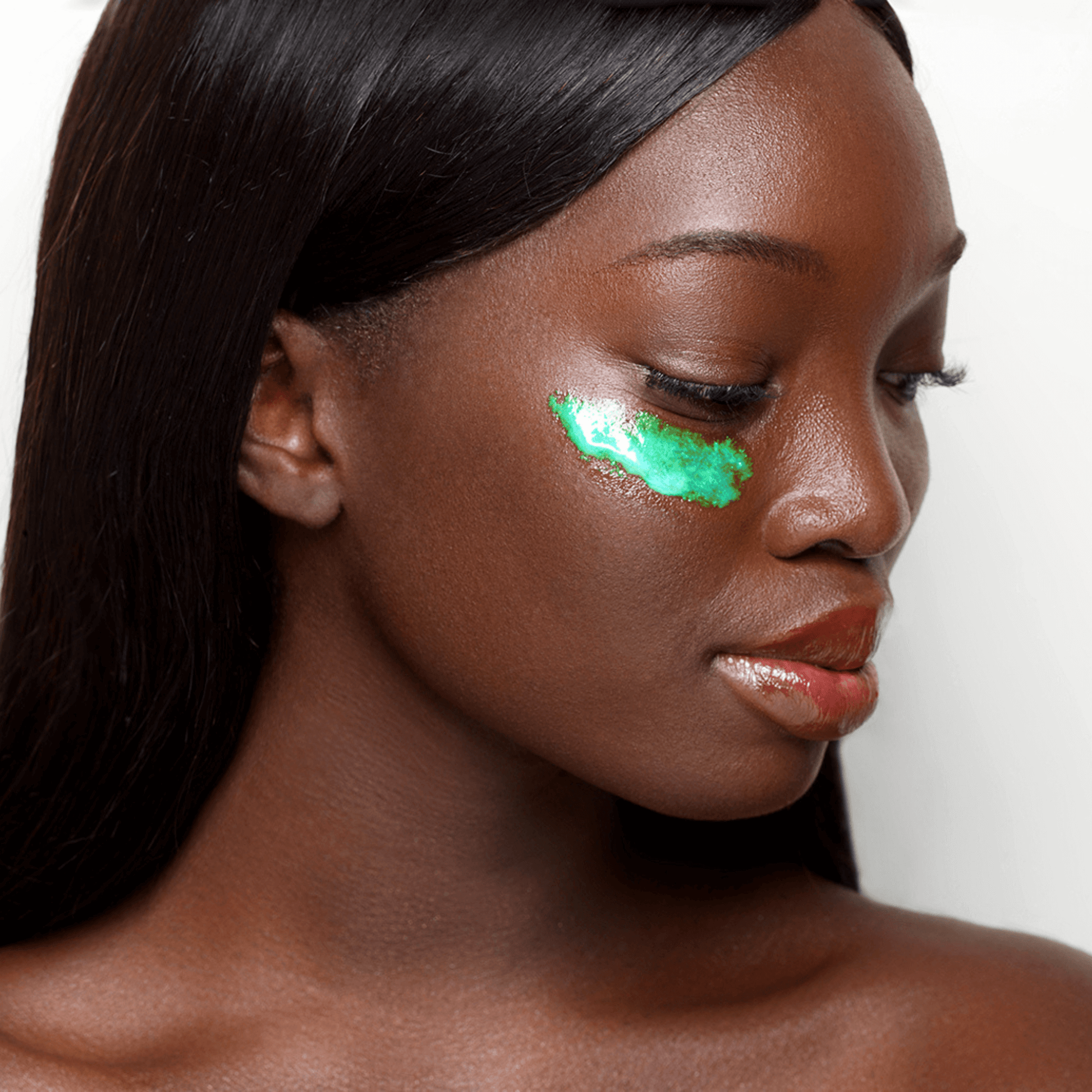 Woman with iridescent green serum on her under eye against a neutral background