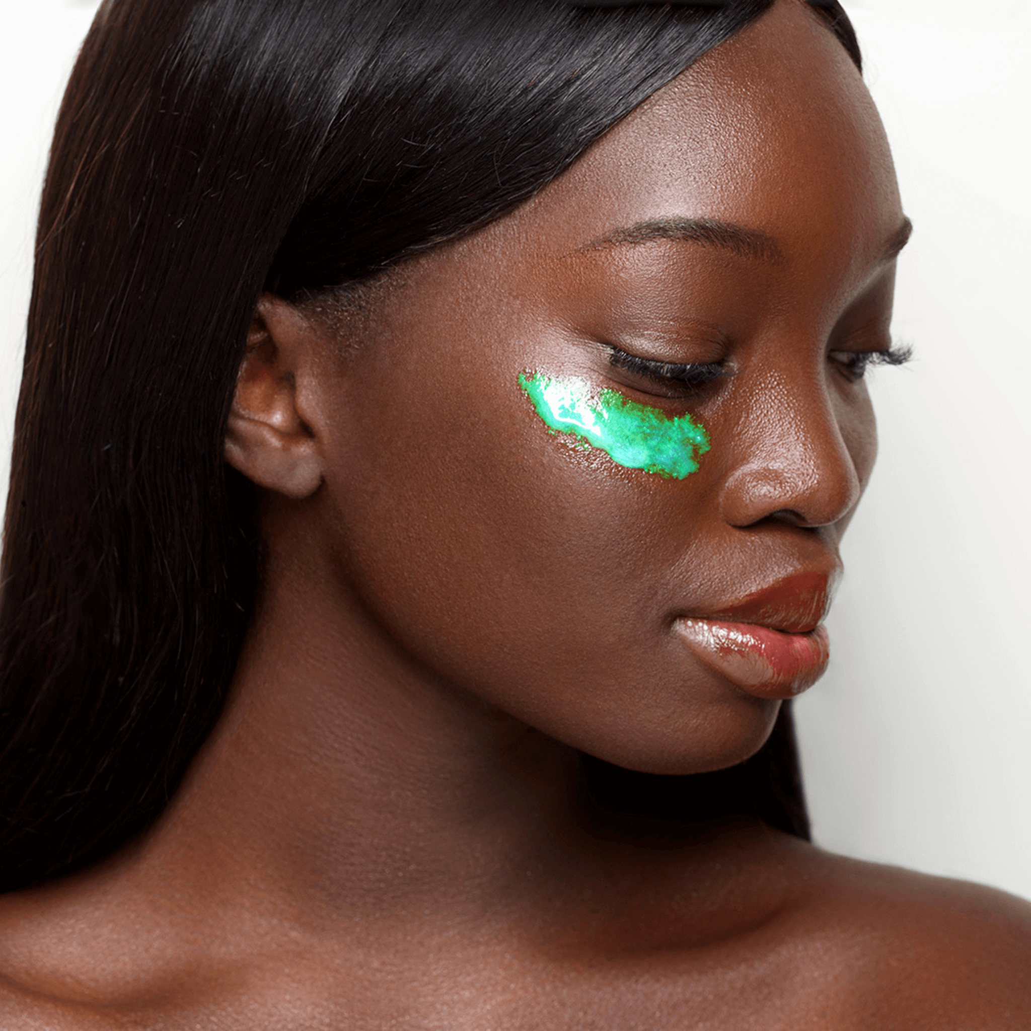 Woman with iridescent green serum on her under eye against a neutral background