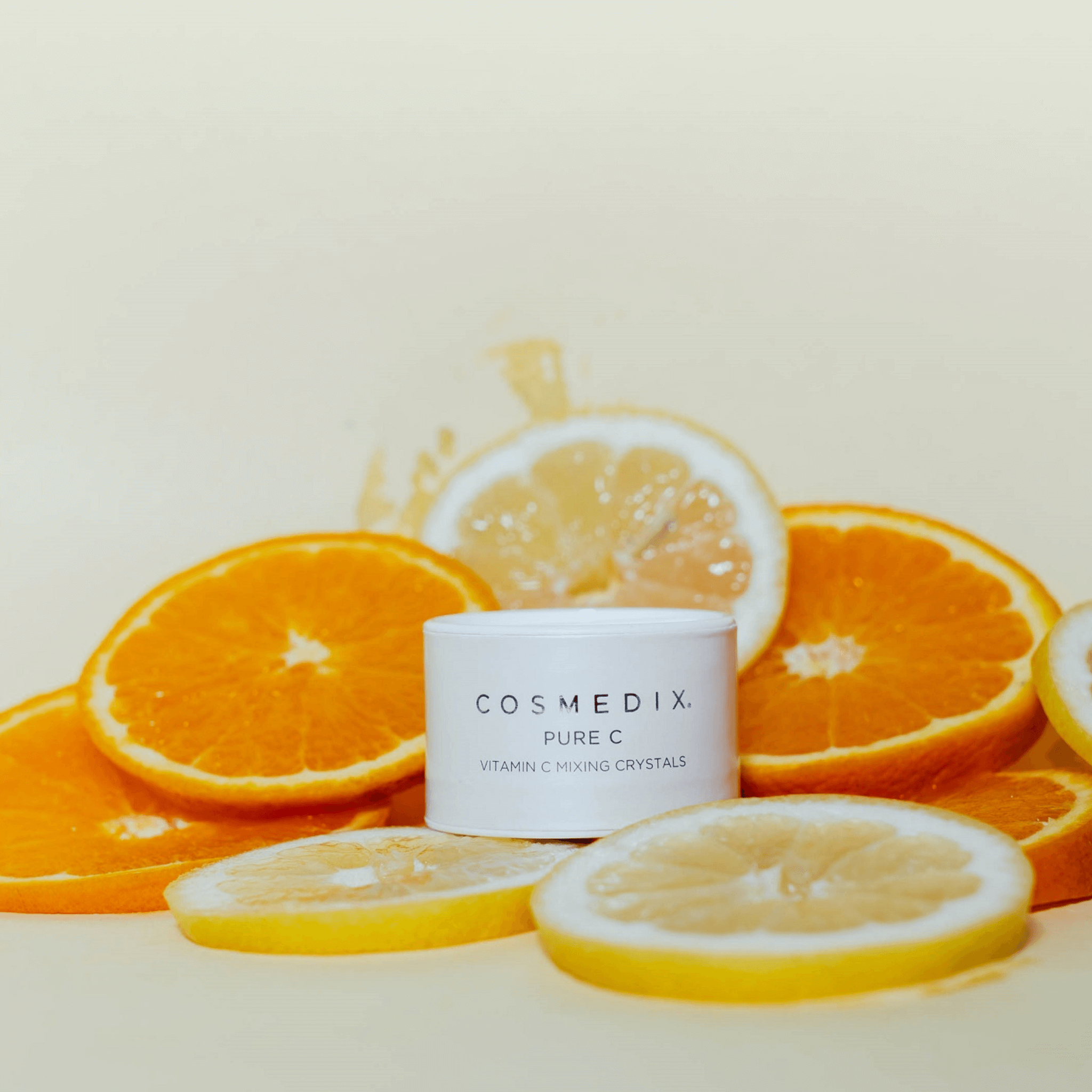 Cosmedix Pure C product with sliced oranges and lemons on a beige background