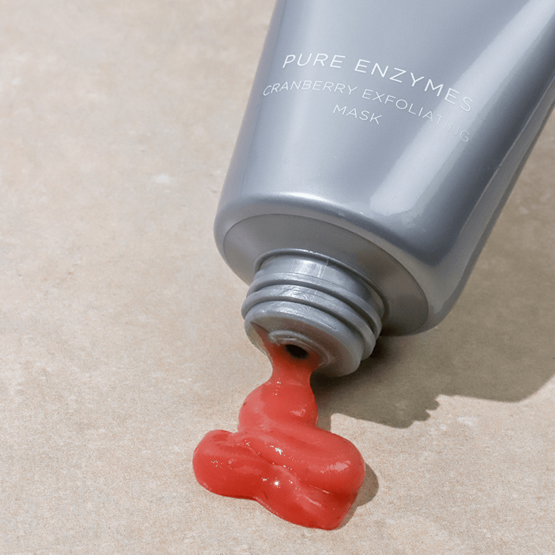 Pure Enzymes cranberry exfoliating mask oozing out of the top on a beige background