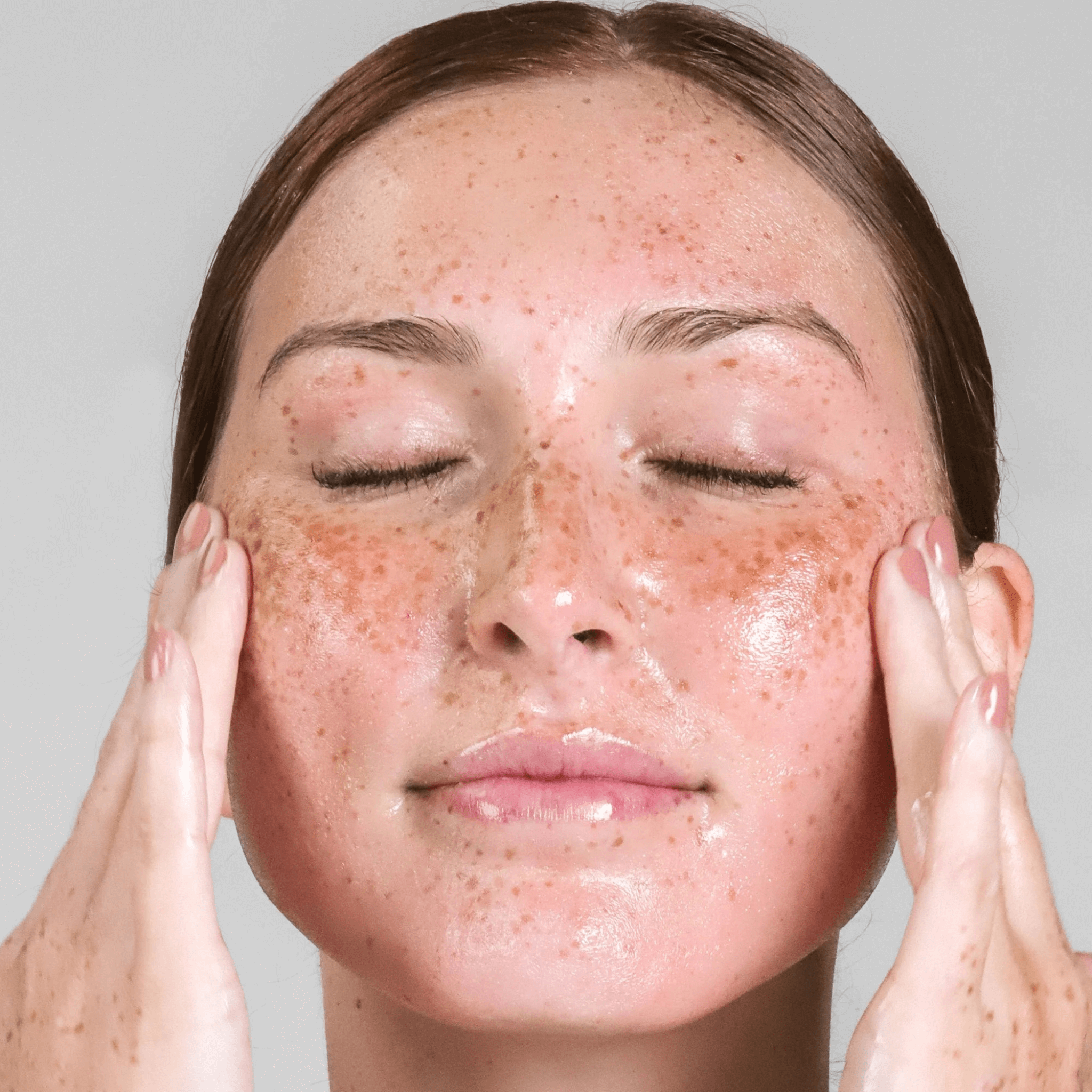 Woman with freckles applying Cosmedix Purity Solution product on her face against a neutral background