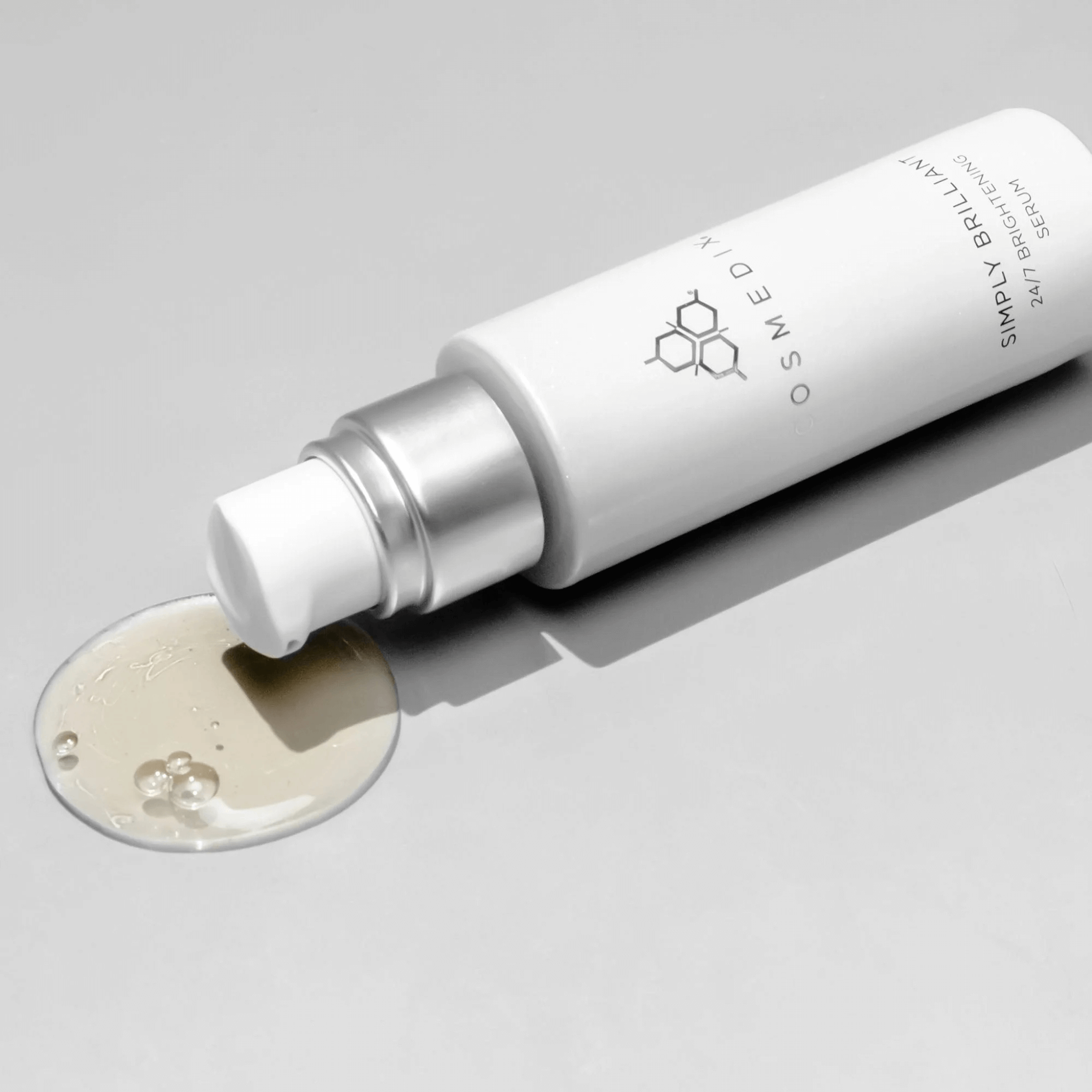Cosmedix serum bottle with a droplet of serum on a grey background