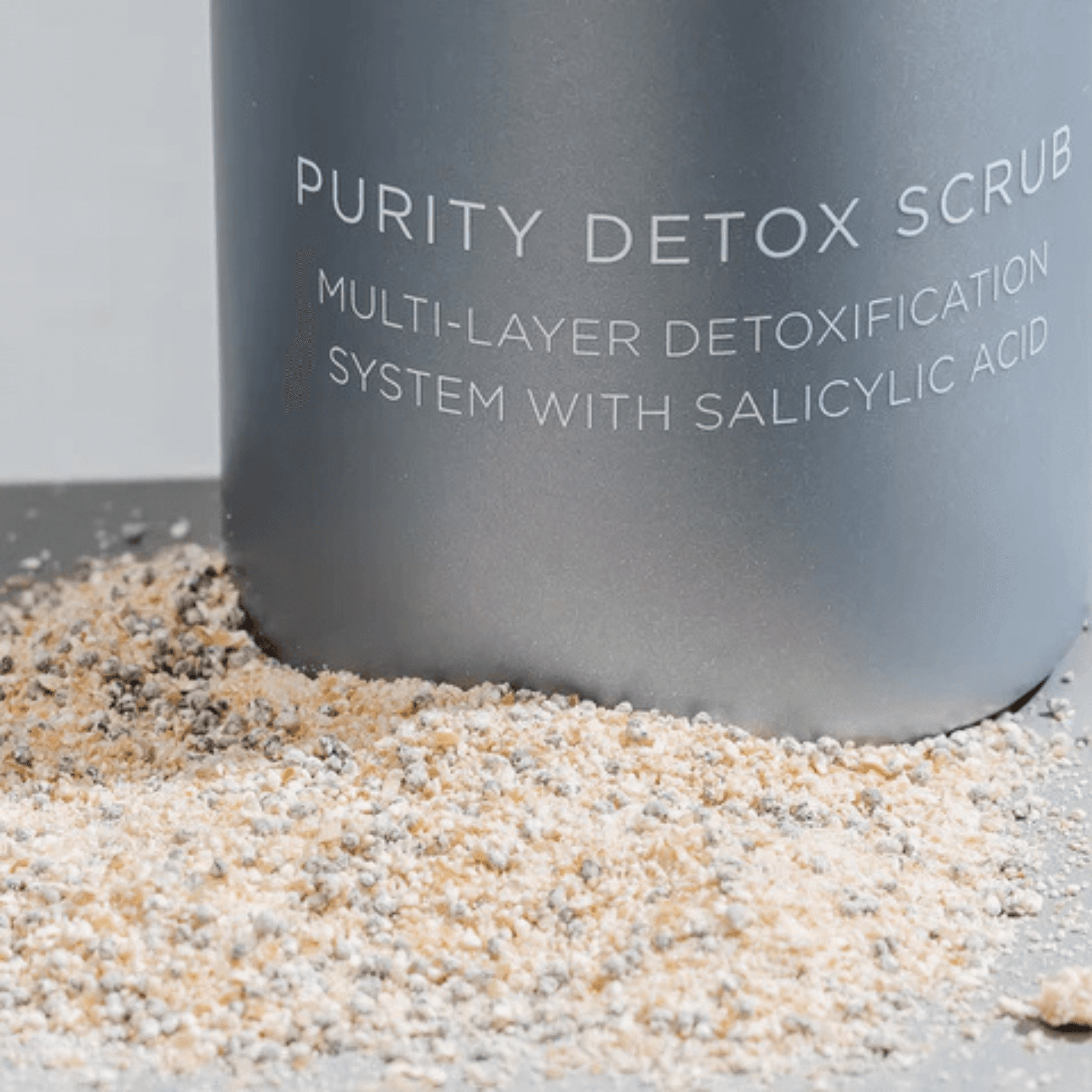 Purity Detox Scrub bottle with sand on a grey background