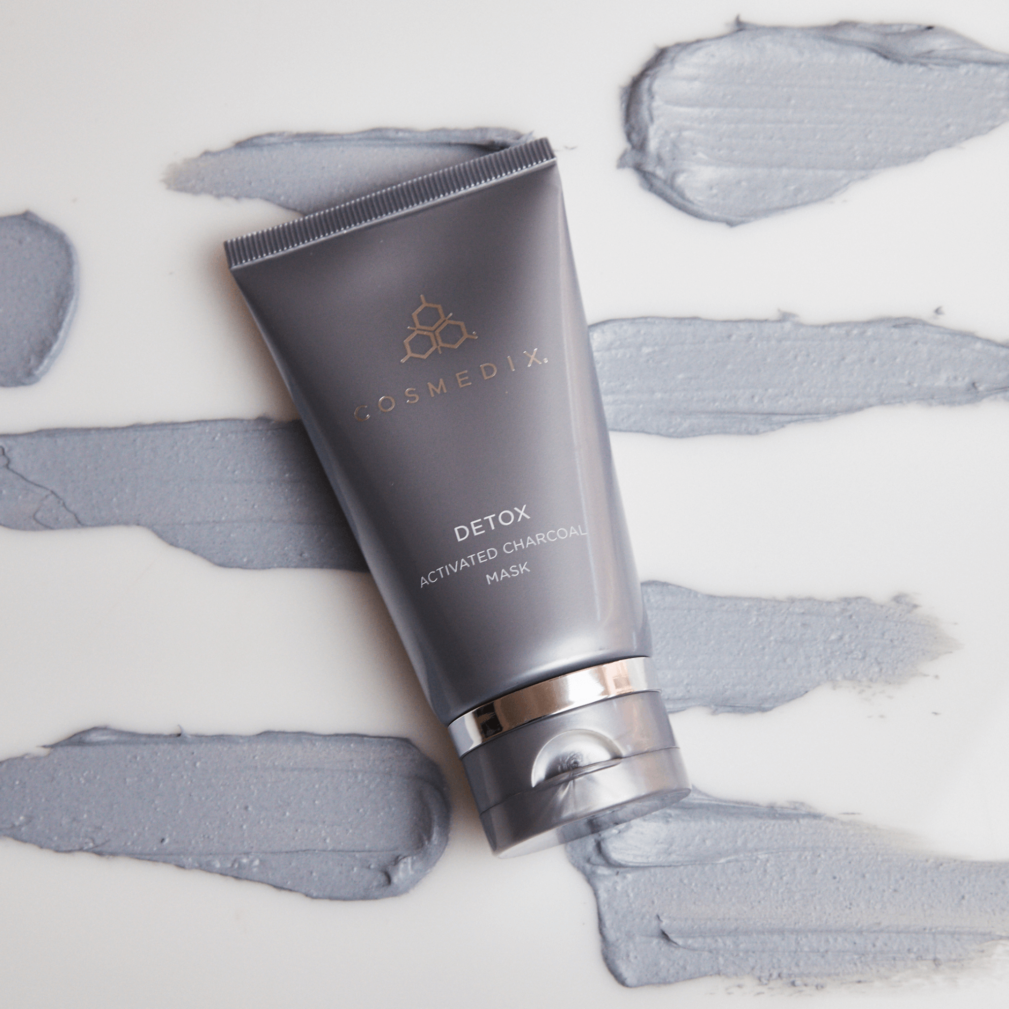 Cosmedix Detox Activated Charcoal Mask tube on a white background with charcoal mask swatches