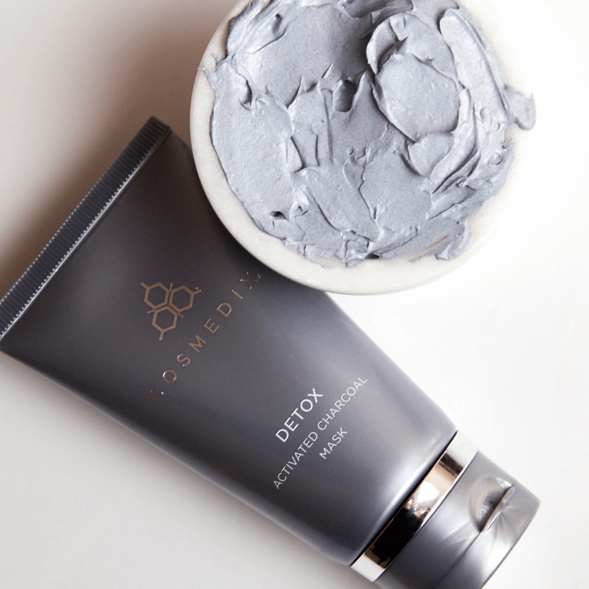 Cosmedix Detox Activated Charcoal Mask with a bowl of mask paste on a light background