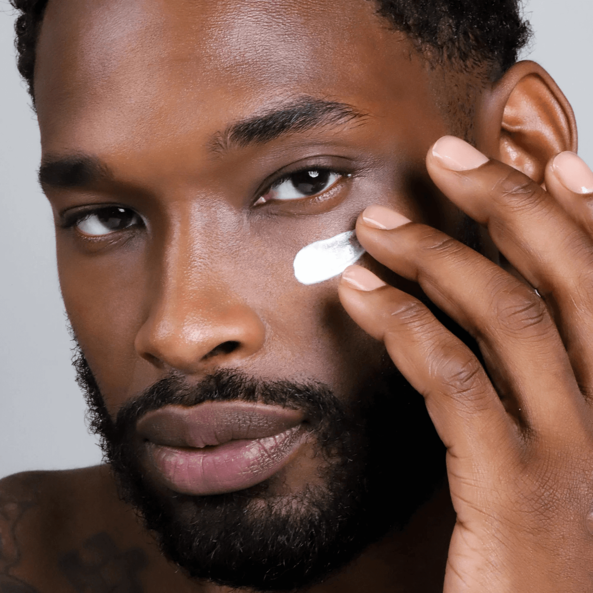 Man applying Cosmedix Eye Genius cream under his eye with a neutral background