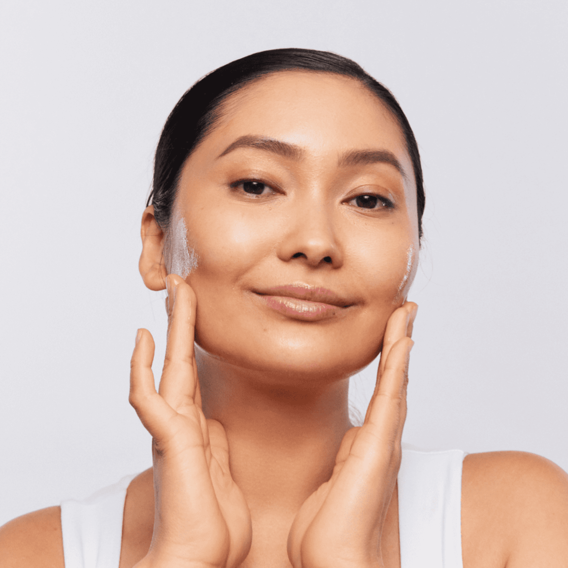 Woman applying Aspect Gentle Clean Cleanser product to her face against a plain background