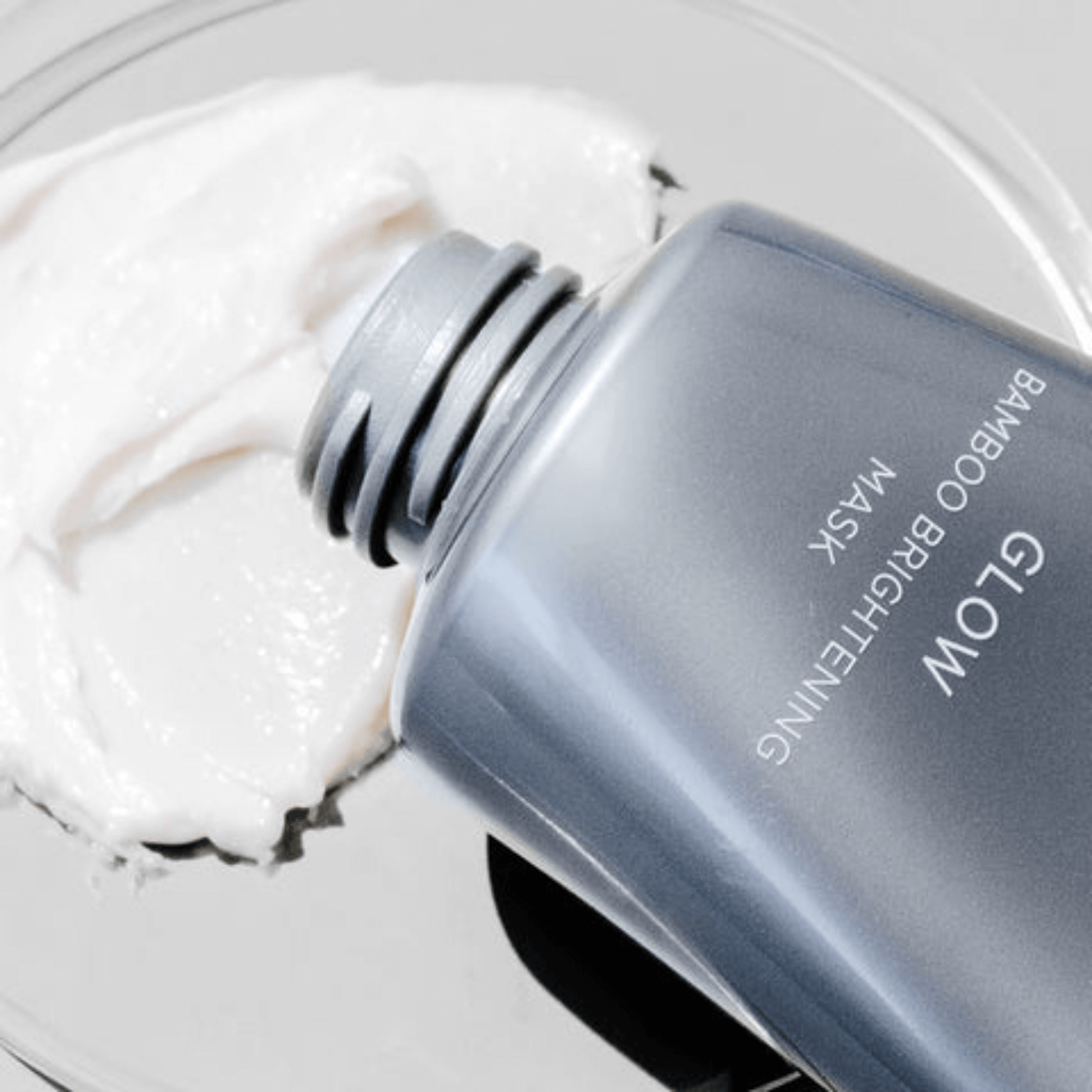 Bottle of Cosmedix Glow Bamboo Brightening Mask with a white mask on a grey background