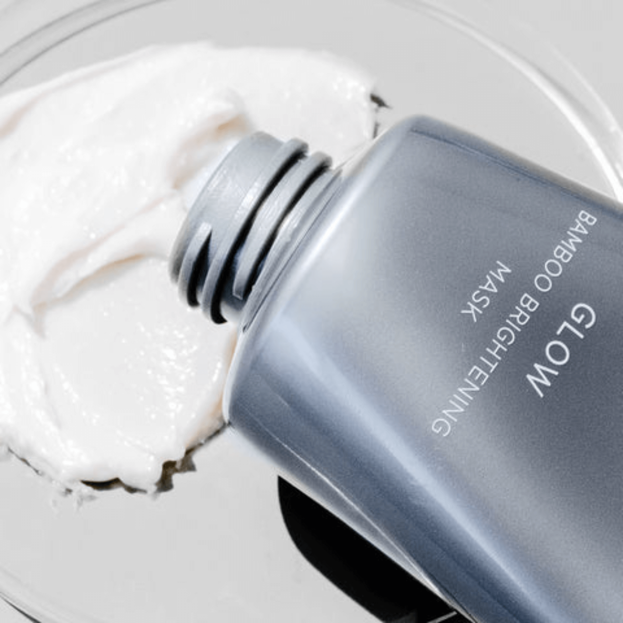 Bottle of Cosmedix Glow Bamboo Brightening Mask with a white mask on a grey background