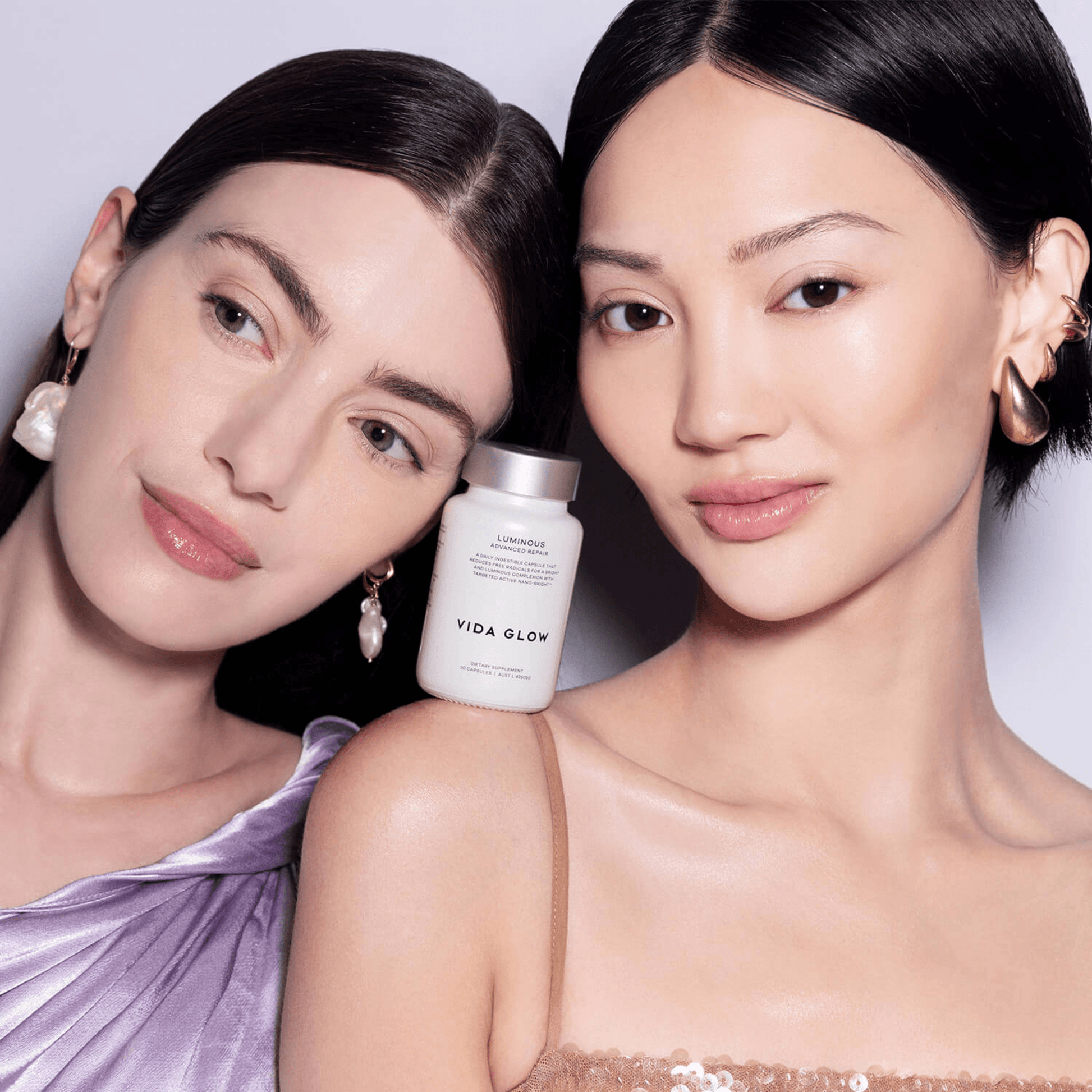 Two women with a 'Vida Glow Luminous' product between them against a light background