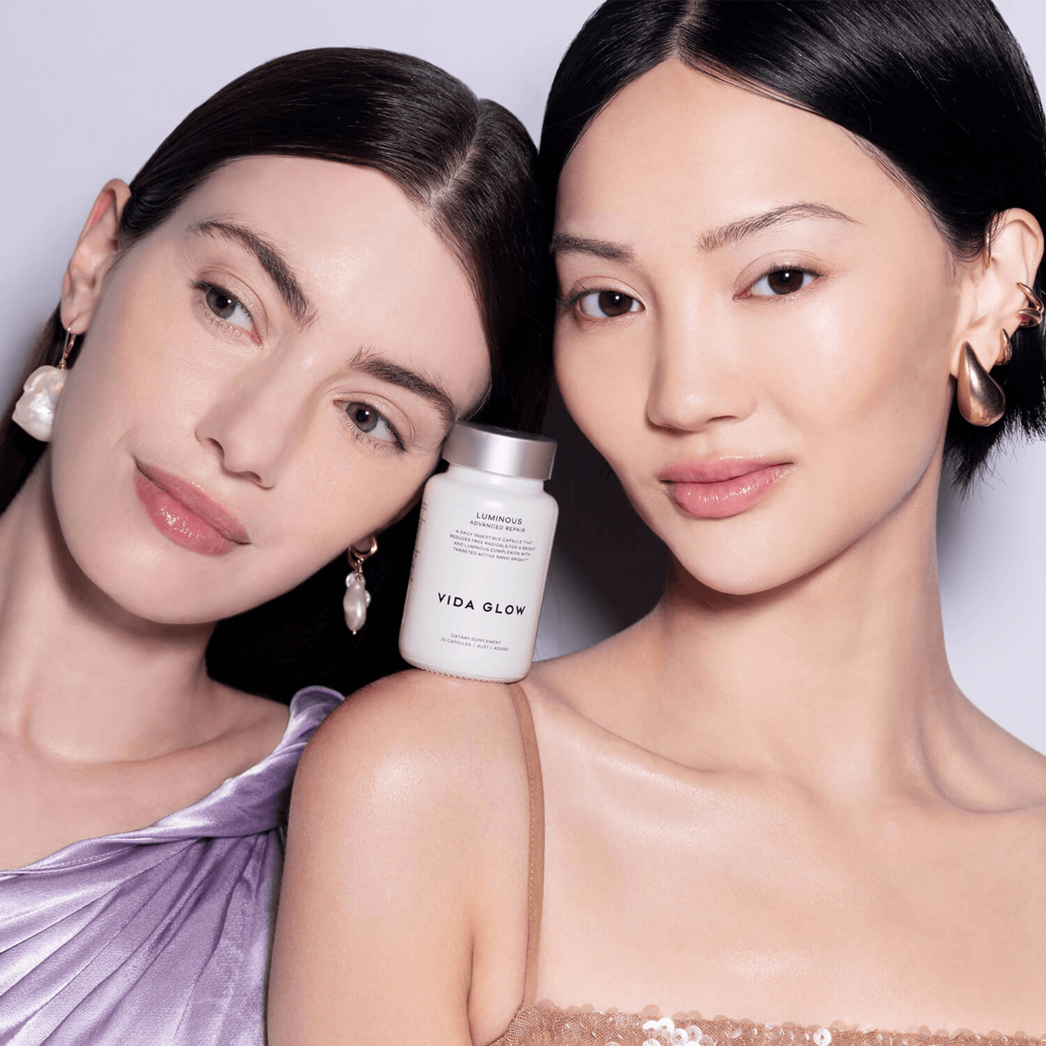 Two women with a 'Vida Glow Luminous' product between them against a light background