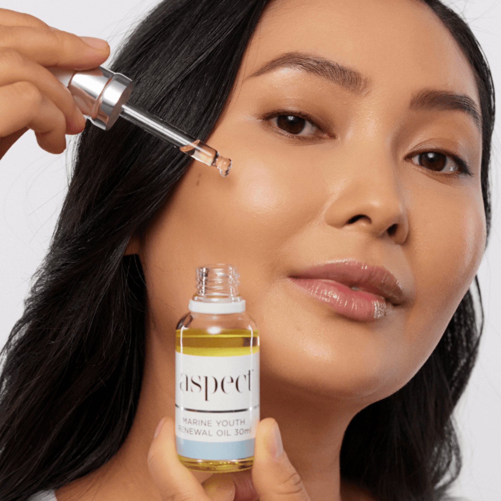Woman applying Aspect Marine Youth Renewal Oil with a dropper on a white background