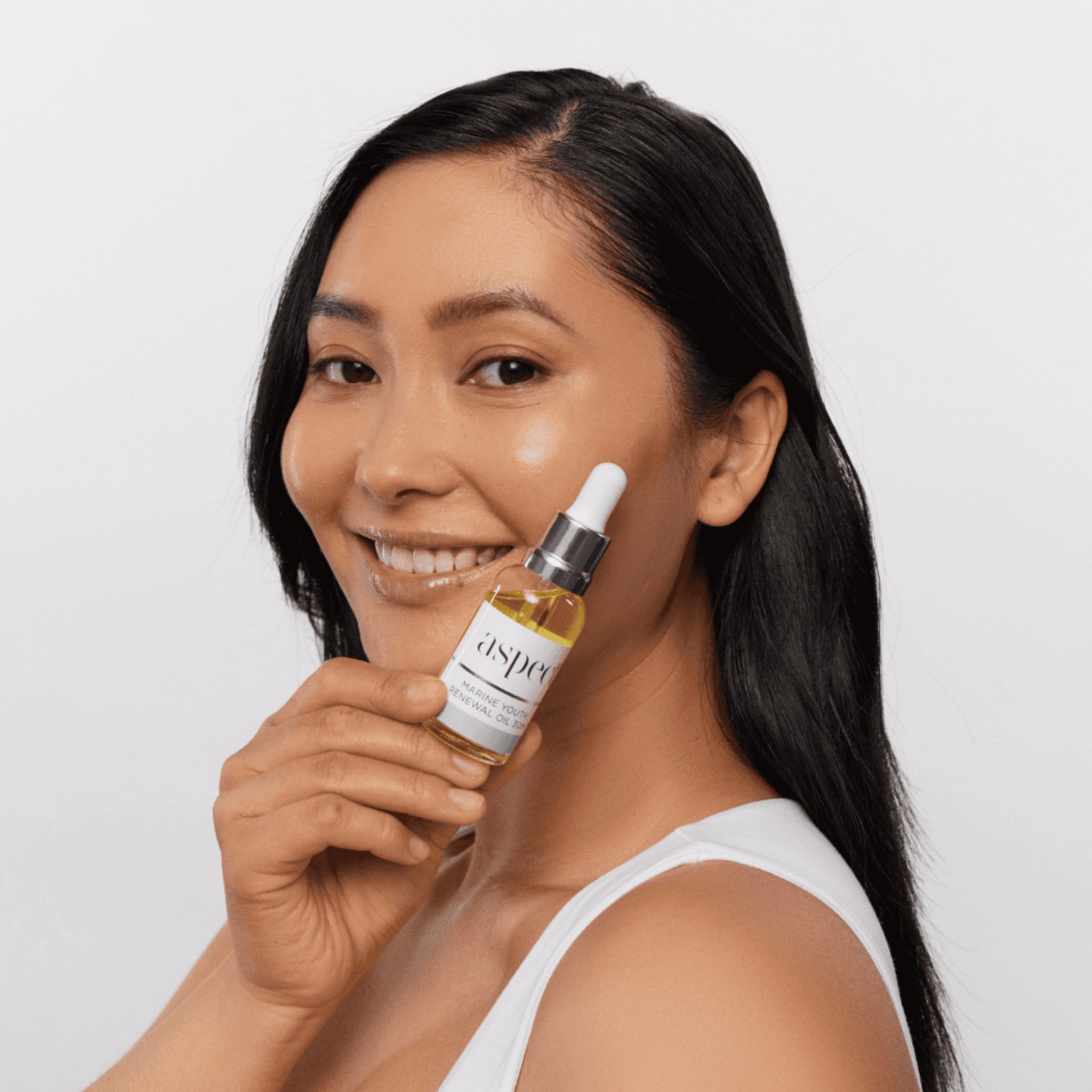 Woman holding a bottle of Aspect youth renewal oil against a white background