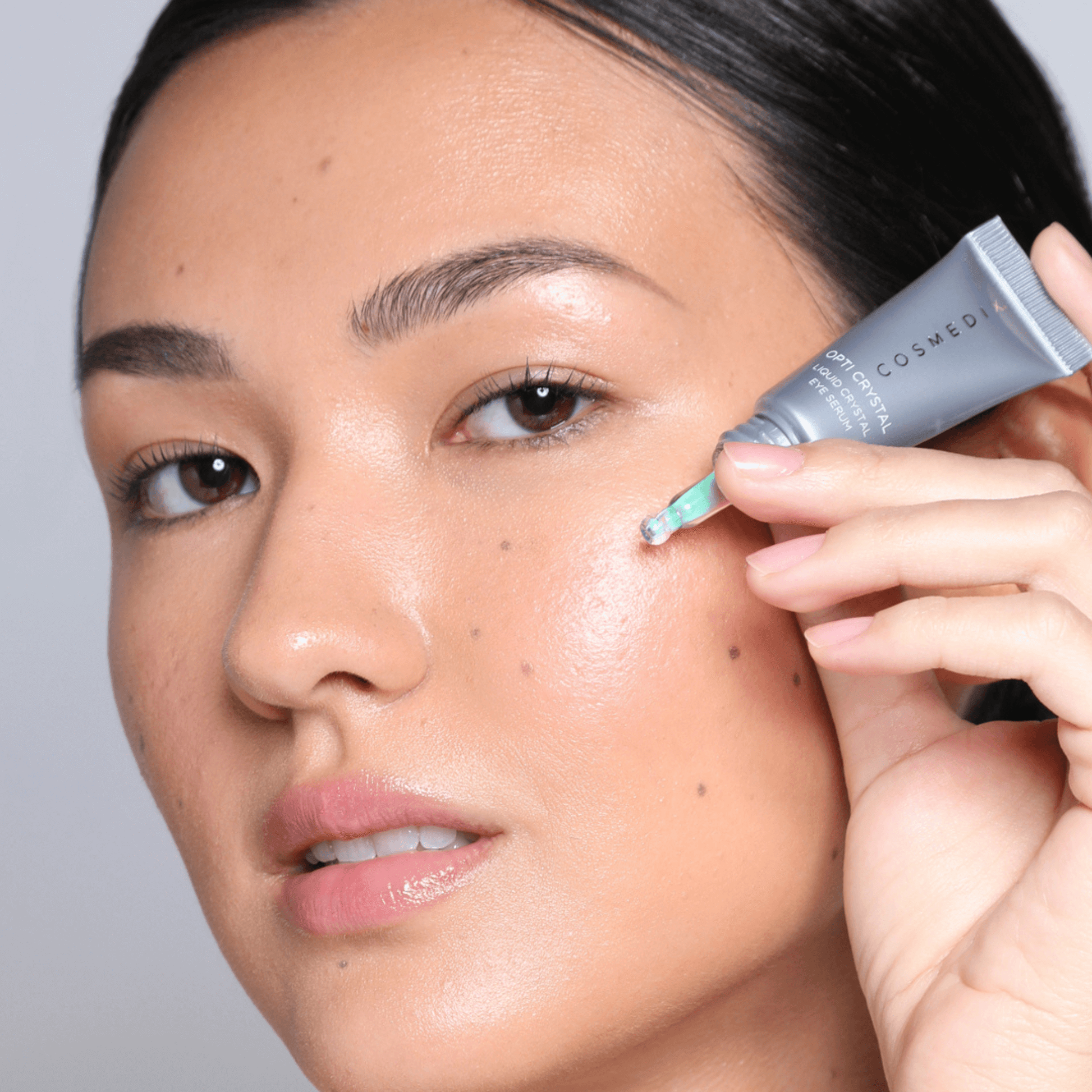 Person applying Cosmedix crystal eye serum to undereye with a grey background