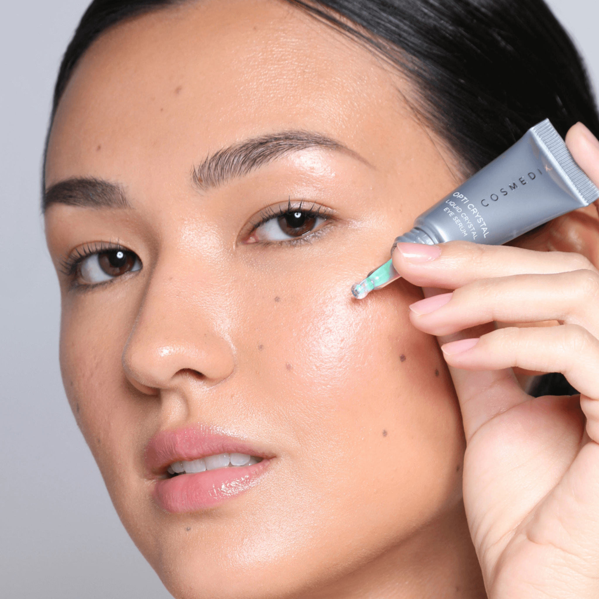 Person applying Cosmedix crystal eye serum to undereye with a grey background
