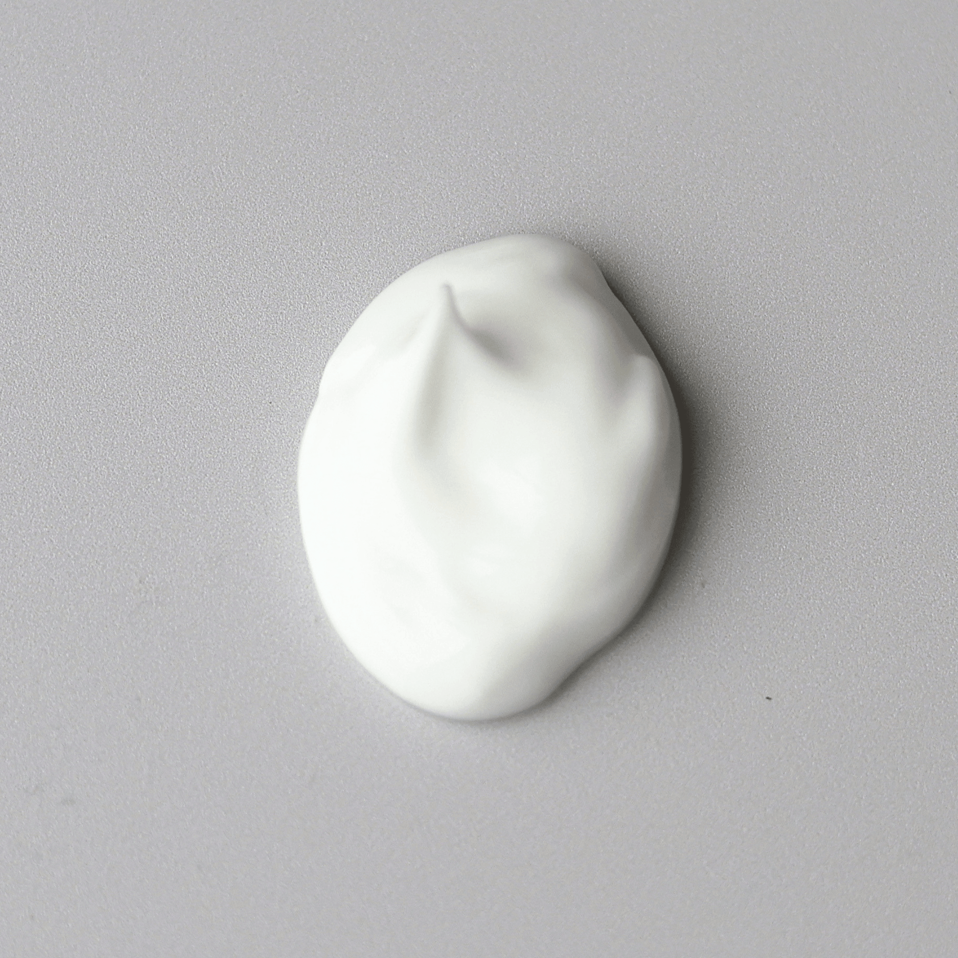 A dollop of thick white Aspect Phytostat 9 cream centered on a plain light grey surface.