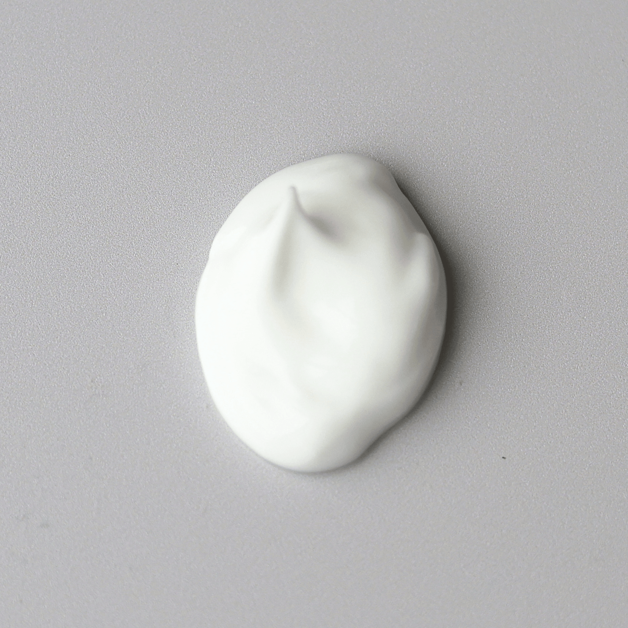 A dollop of thick white Aspect Phytostat 9 cream centered on a plain light grey surface.