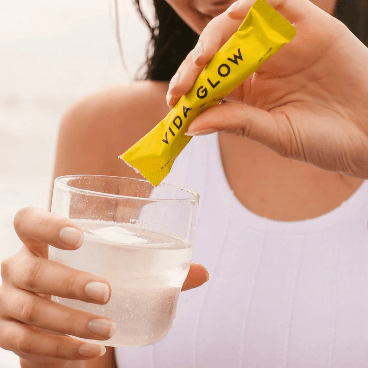 Model holding and pouring Pineapple Vida Glow collagen from a sachet into a glass of water
