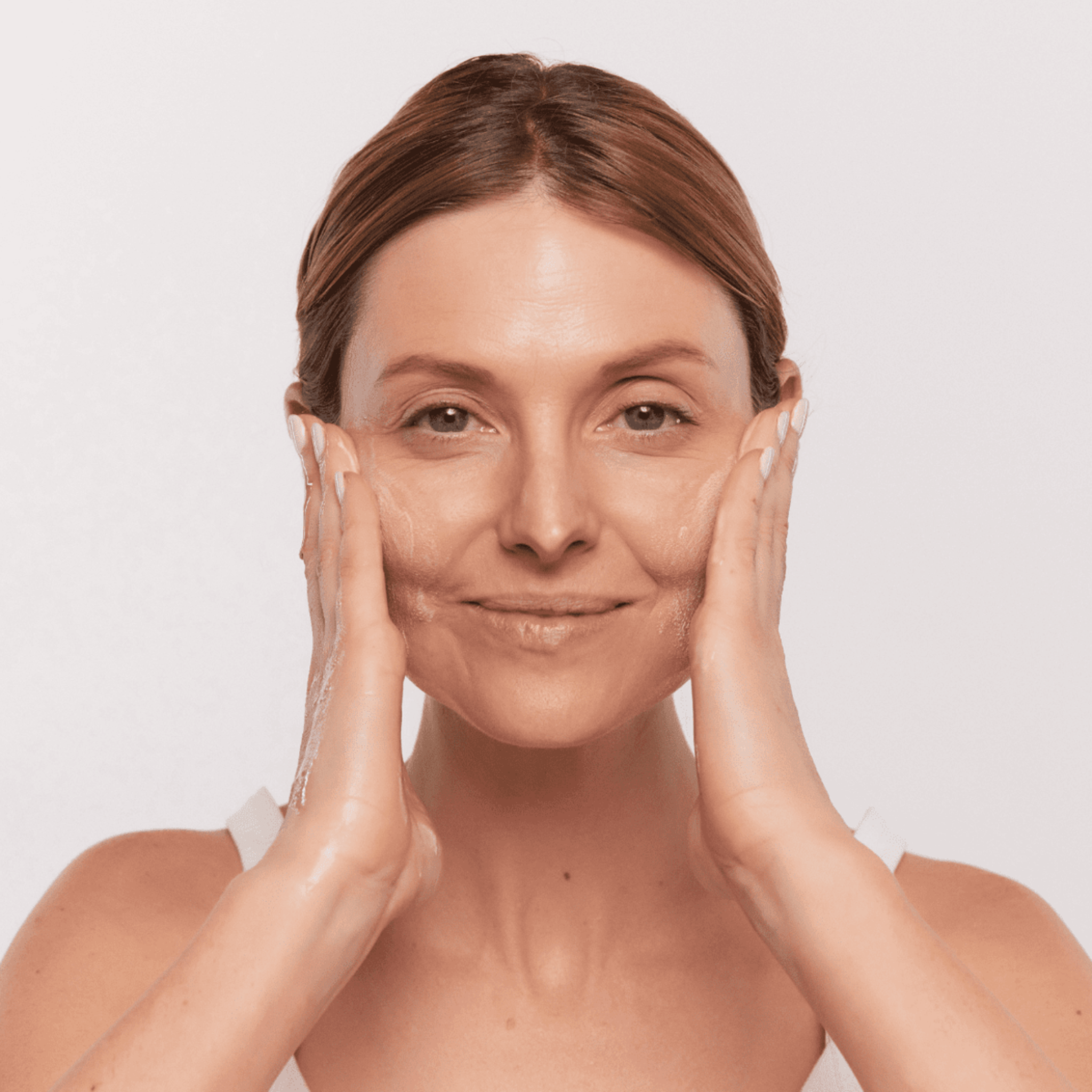 Woman with smooth skin using Aspect Purastat 5 cleanser against a light background