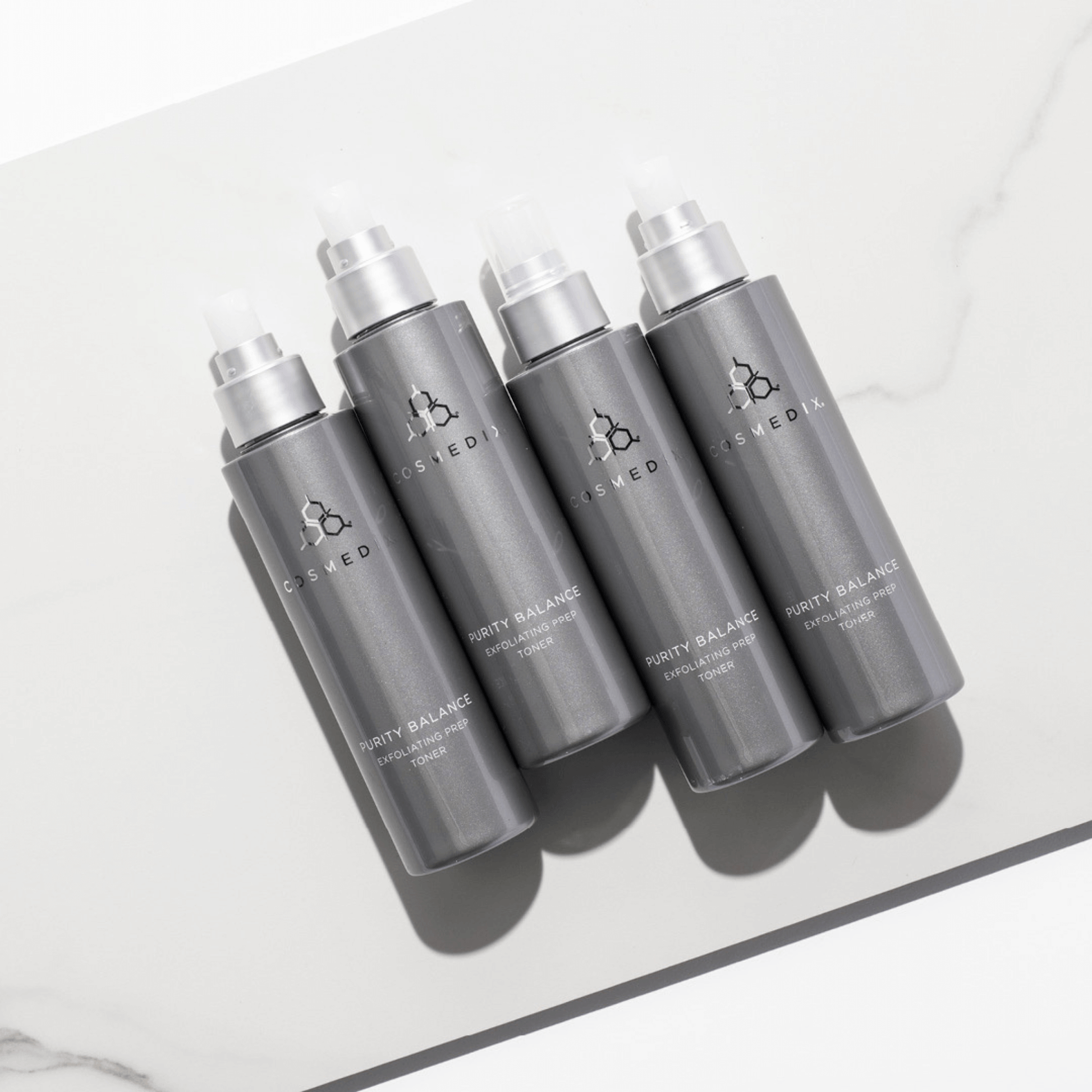 Five grey bottles of Cosmedix Purity Balance toner prep with silver caps on a light grey background
