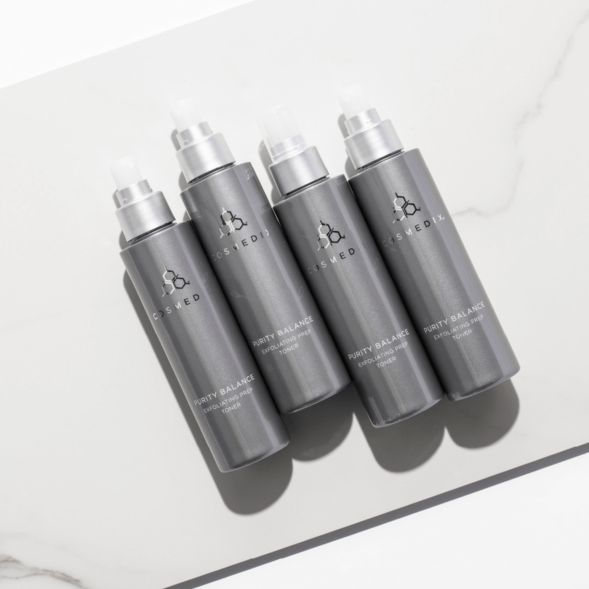 Five grey bottles of Cosmedix Purity Balance toner prep with silver caps on a light grey background