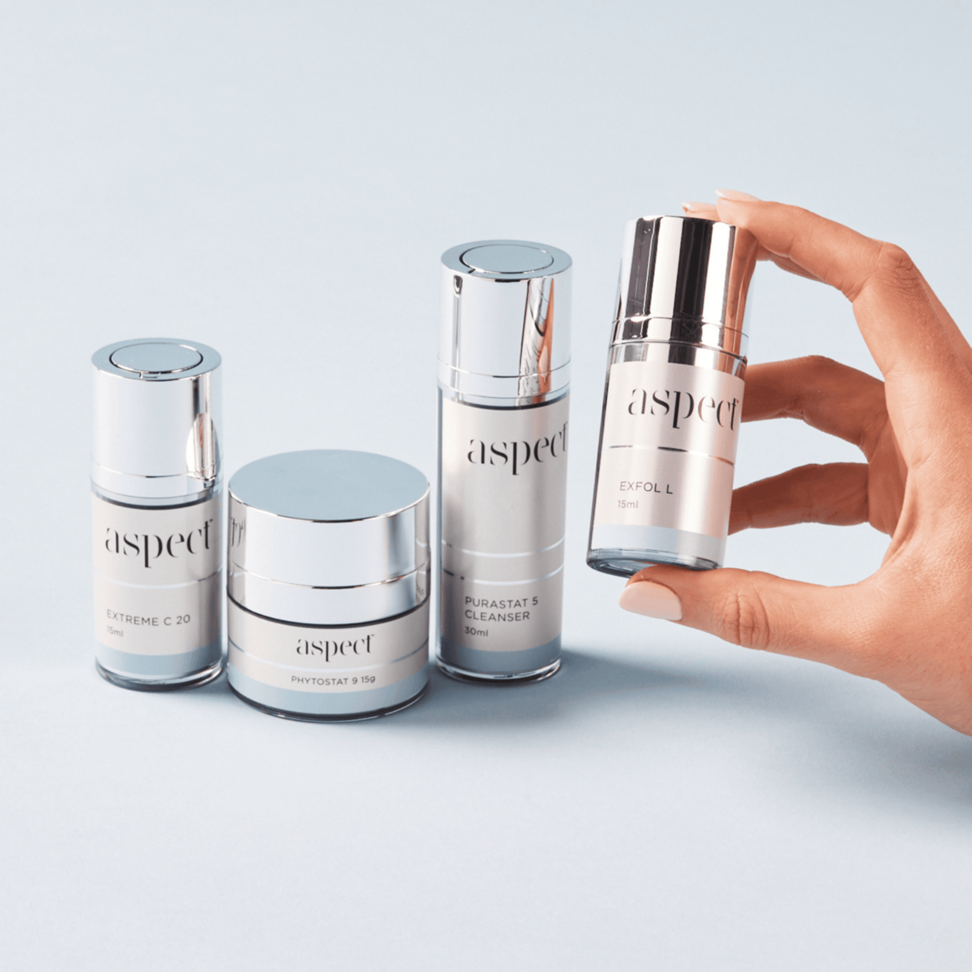 Hand holding an Aspect skincare product with other Aspect skincare products on a light background