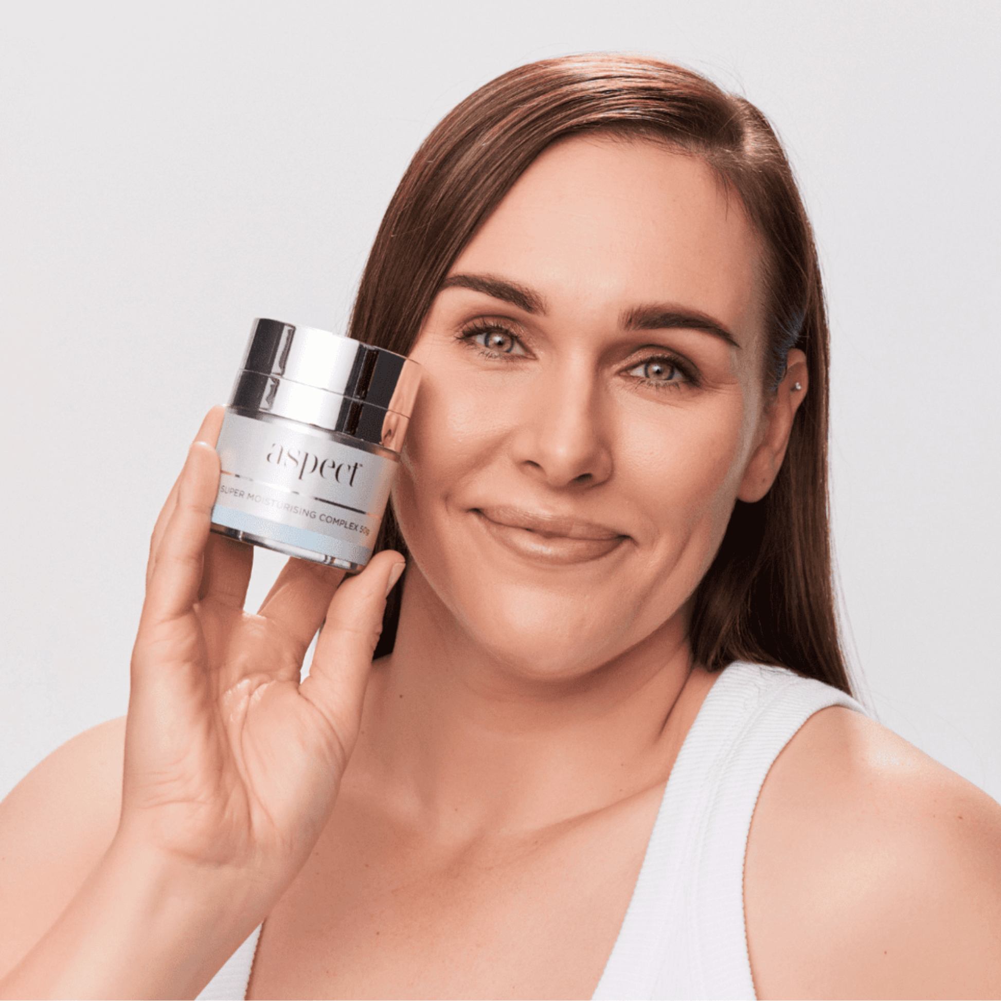 Woman holding a jar of aspect Super Moisturising complex cream against a plain background