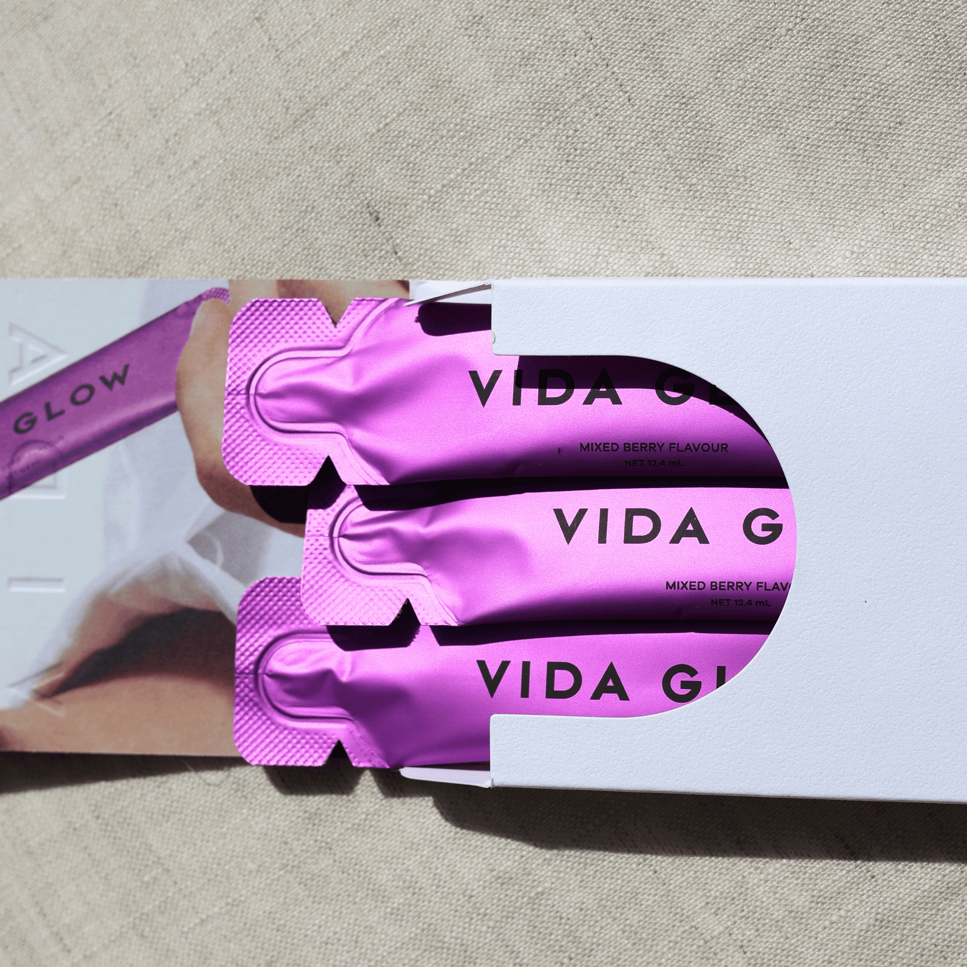 Vida Glow product packaging with purple sachets on a beige surface