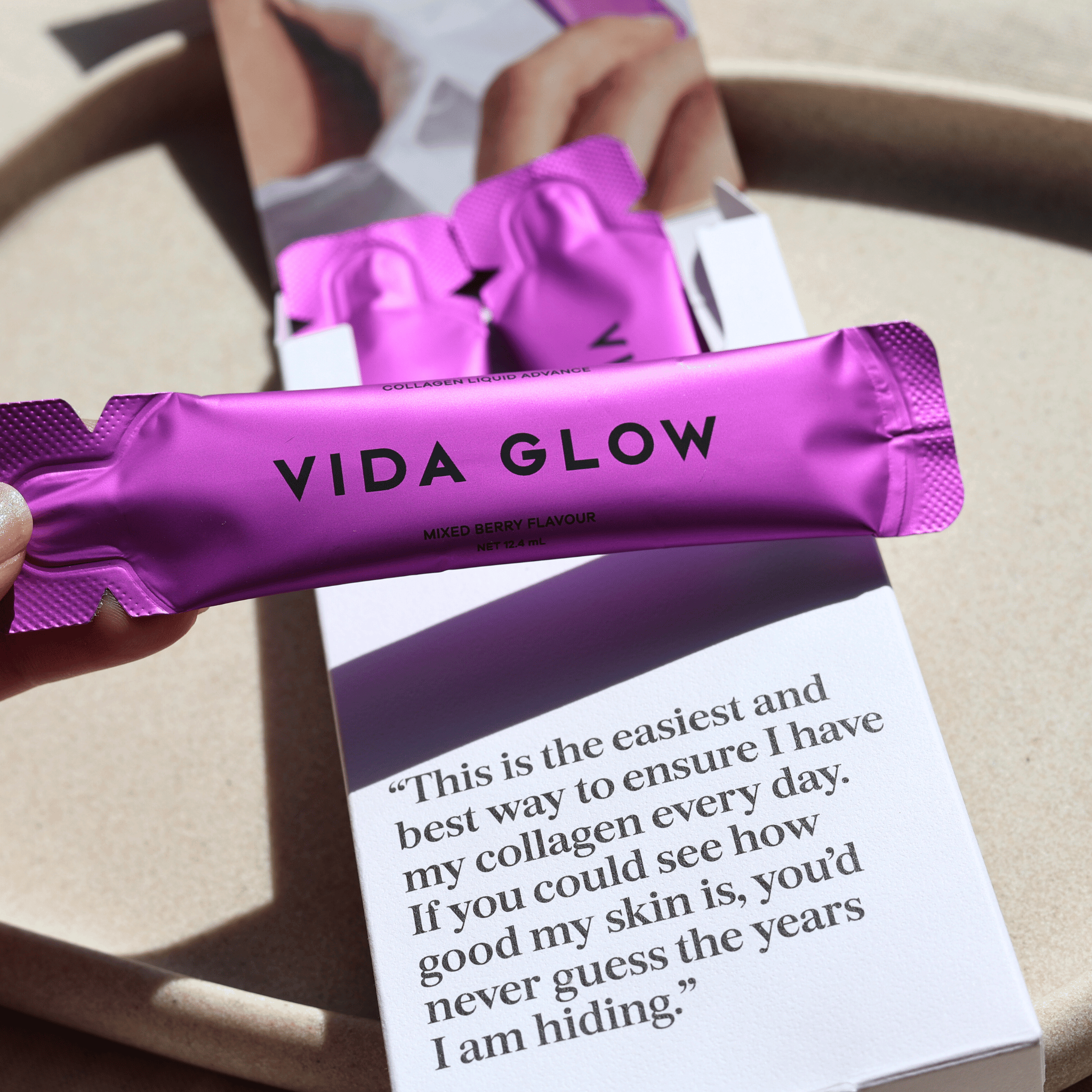 Purple Vida Glow supplement packet held by a hand with a quote underneath.