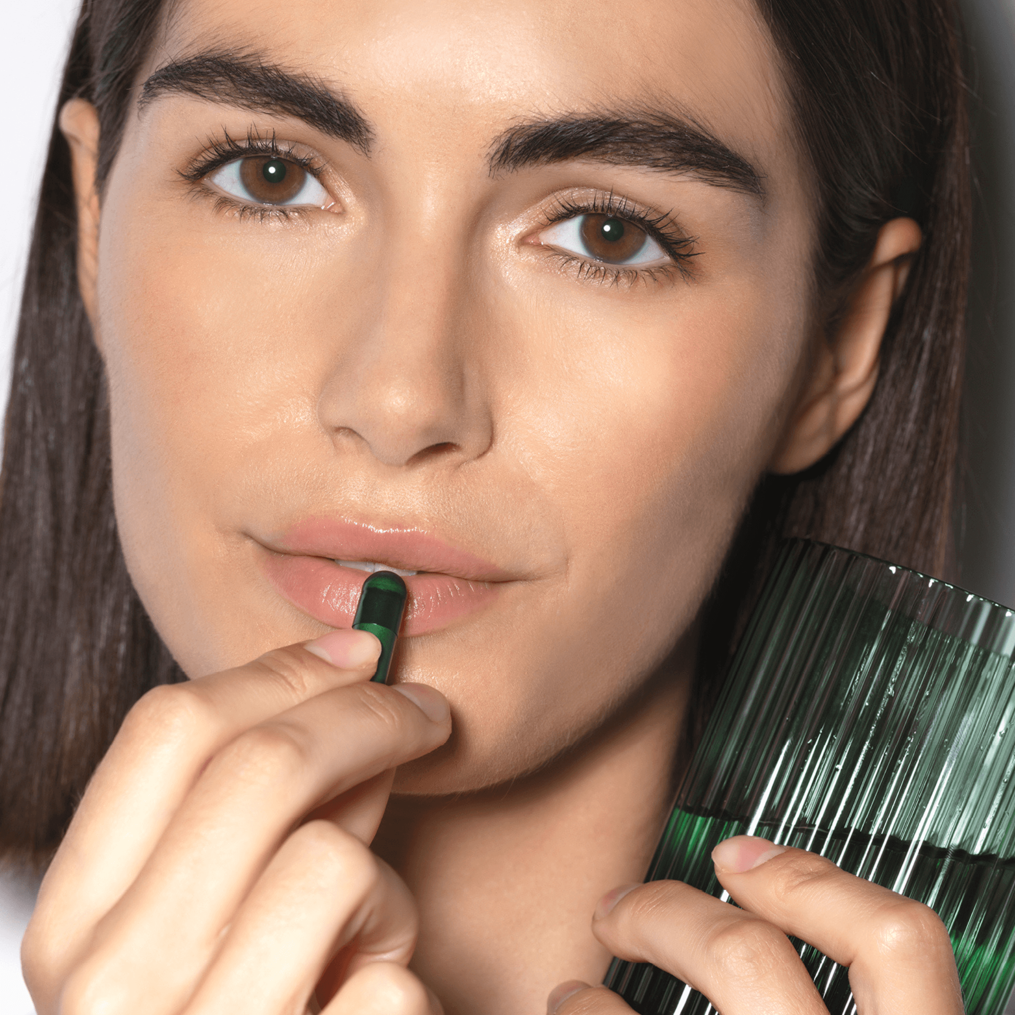 Woman holding a Vida Glow green radiance+ capsule and green glass with water