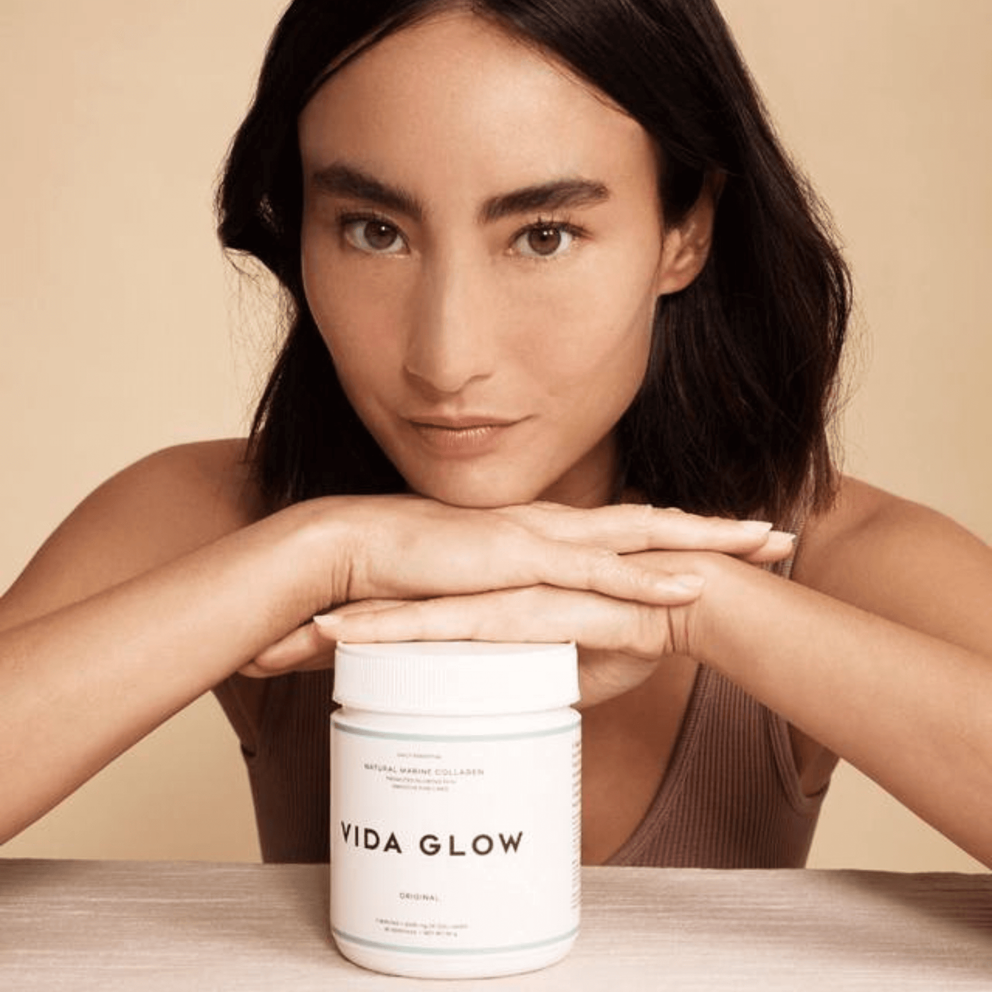 Vida Glow collagen powder 90g tub with model resting hands on top of tub