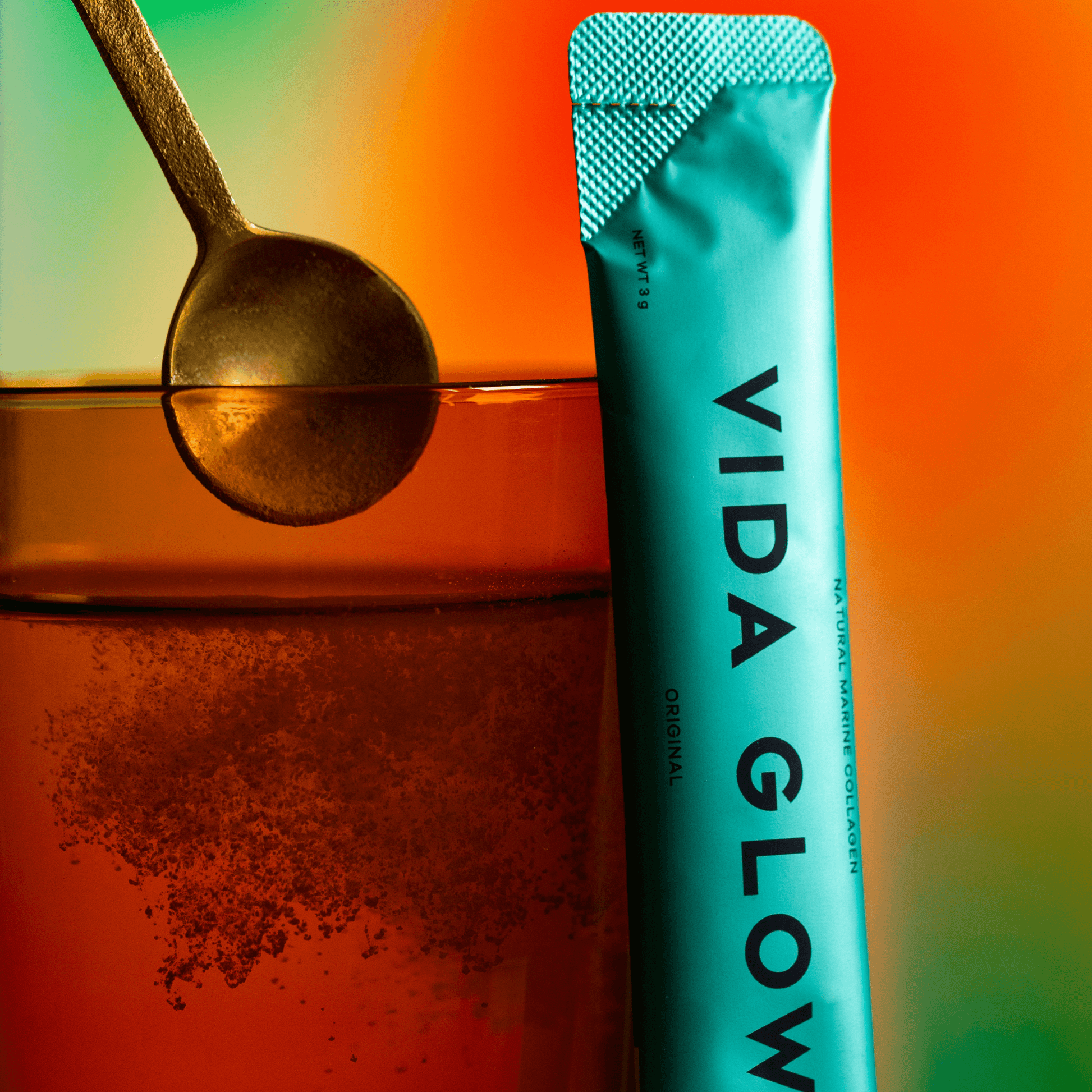 Vida Glow original flavour mixed with a gold spoon in water on orange and green background