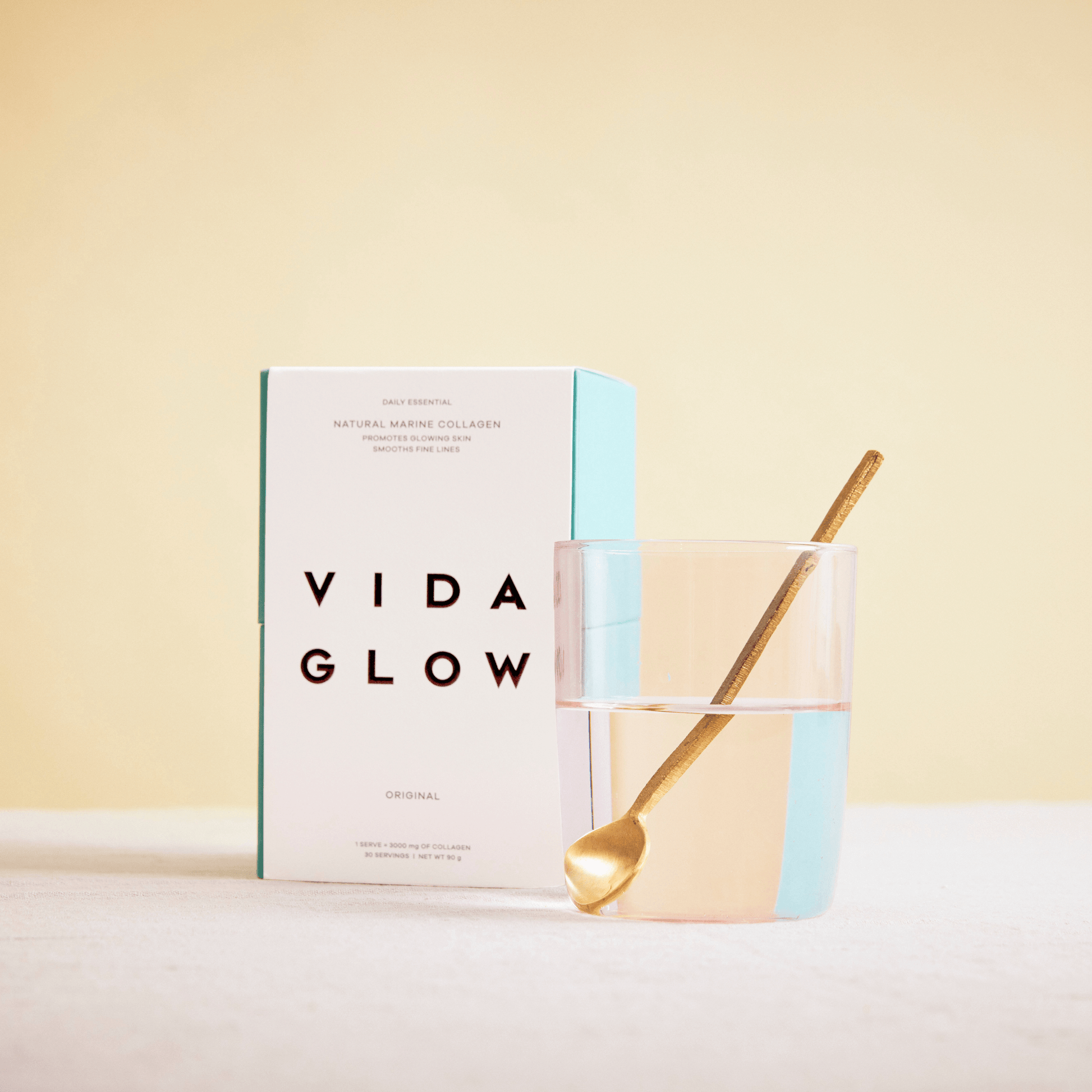 Vida Glow original product box with spoon in a glass of water on yellow background