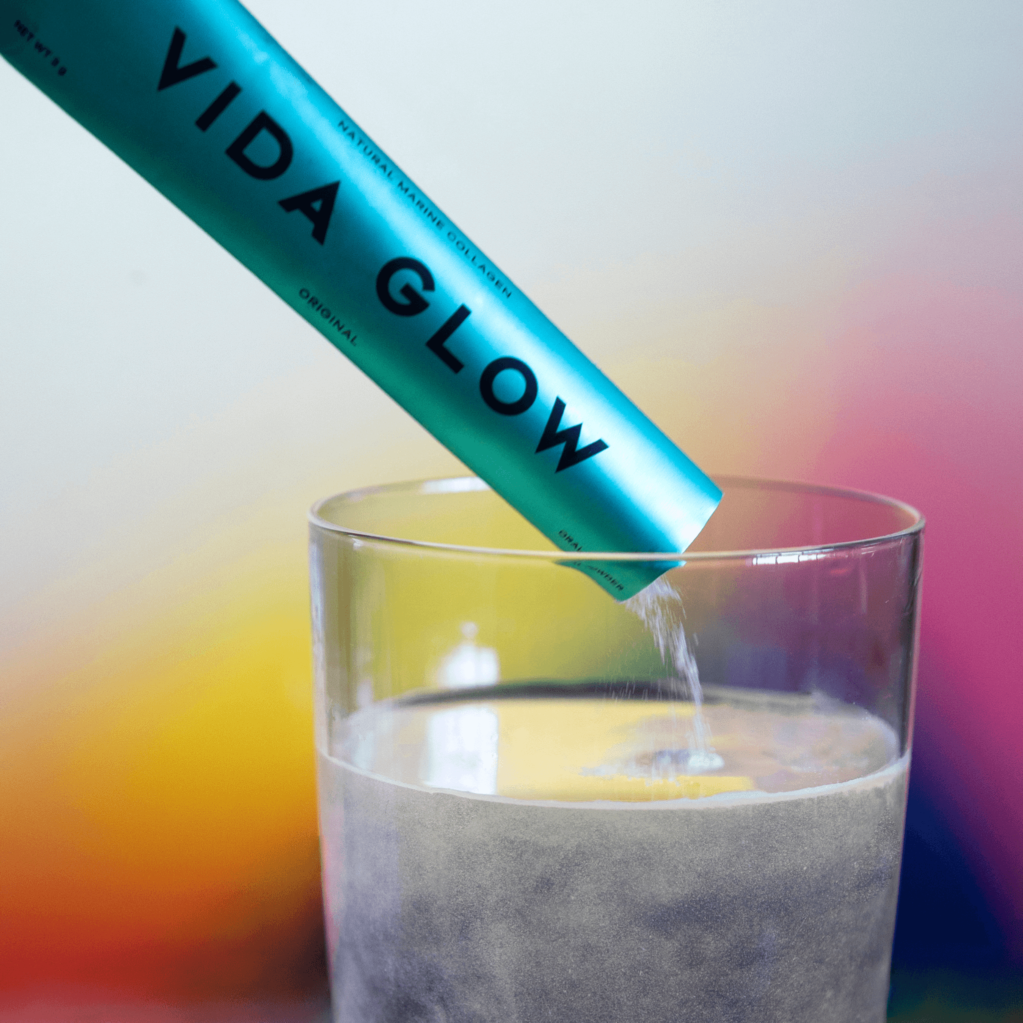 Vida Glow original sachet poured into glass of water on multicoloured background